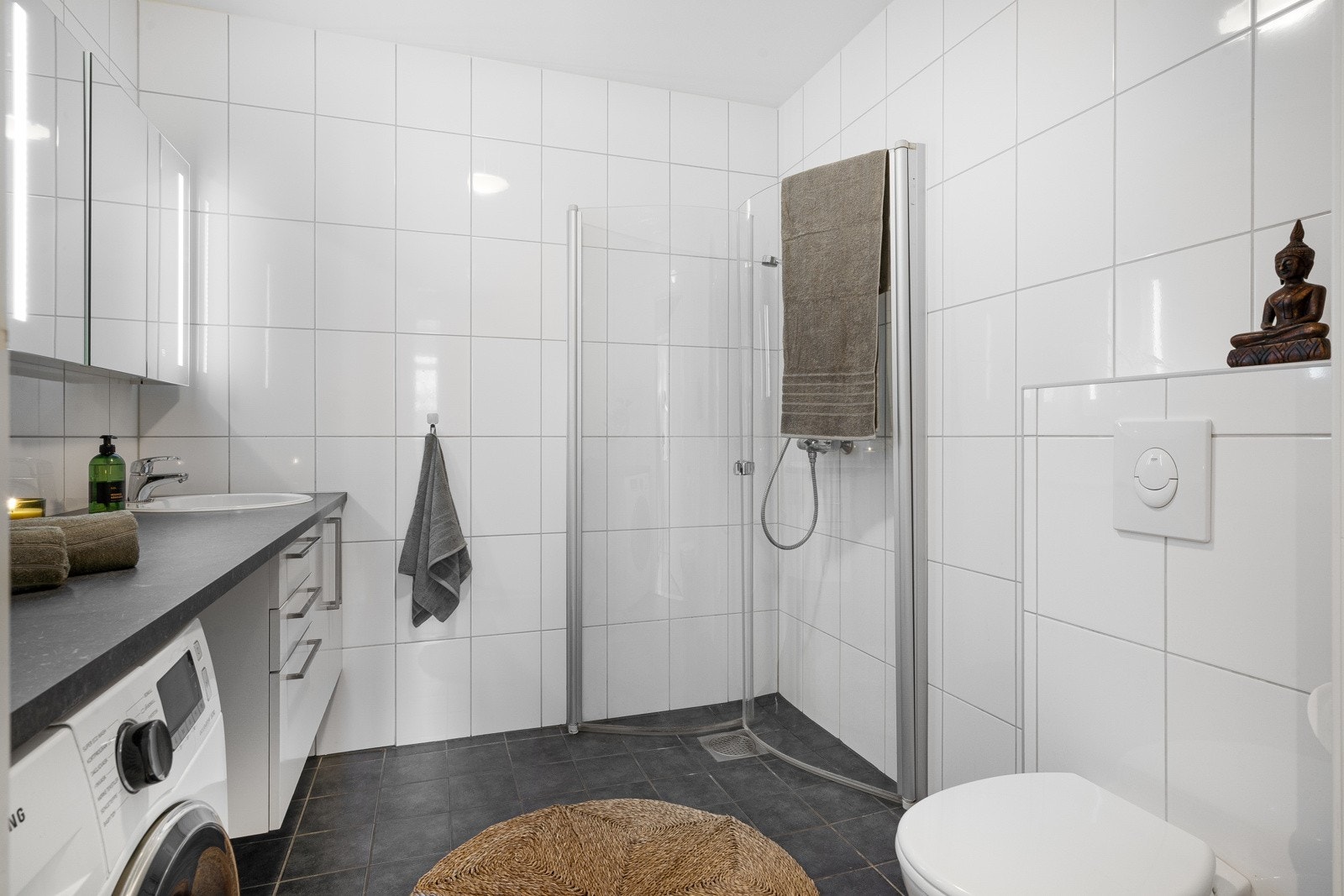 Badet er utstyrt med varmekabler i gulv, innfellbare dusjdører, vegghengt toalett og opplegg for vaskemaskin Galleribilde