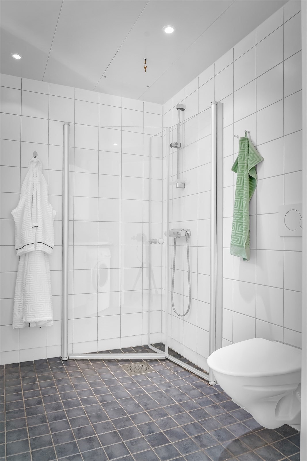 Videre er det servant med underskap, speil med belysning over og skapinnredning på vegg. Opplegg for vaskemaskin. Galleribilde