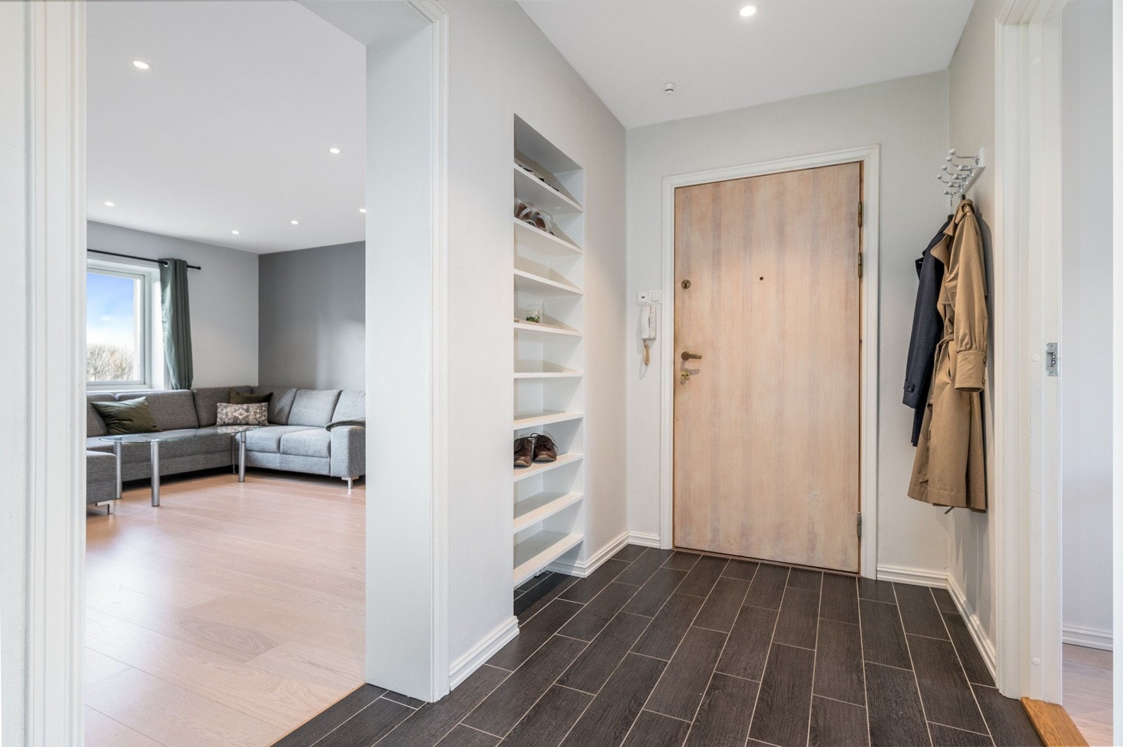 Entréen har mørke fliser på gulv med gulvvarme, lysmalte overflater og downlights i himlingen. Montert porttelefon på vegg og sikringsskap med automatsikringer i felles trapperom. Galleribilde