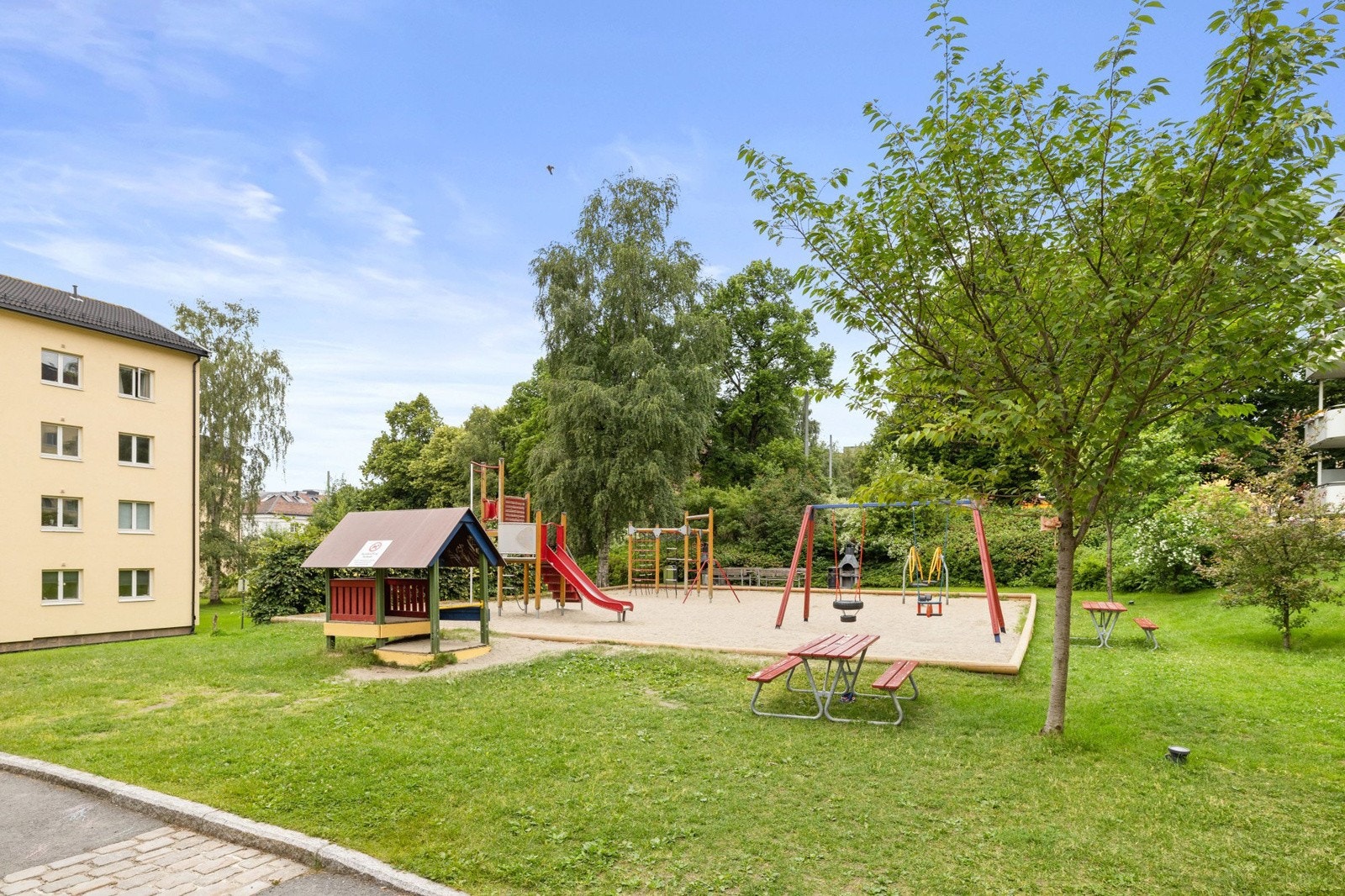 Stedvis prydbusker og store trær, lekeplass og uteplasser rundt blokkene. Galleribilde