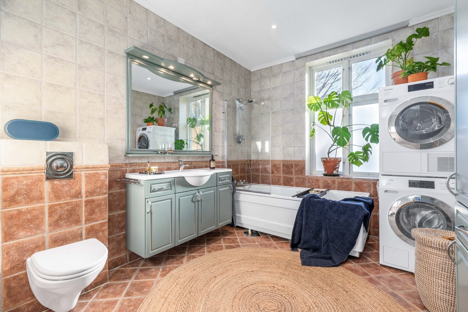 Flislagt baderom med varme i gulv og et stort vindu som byr på morgensolens stråler. Galleribilde