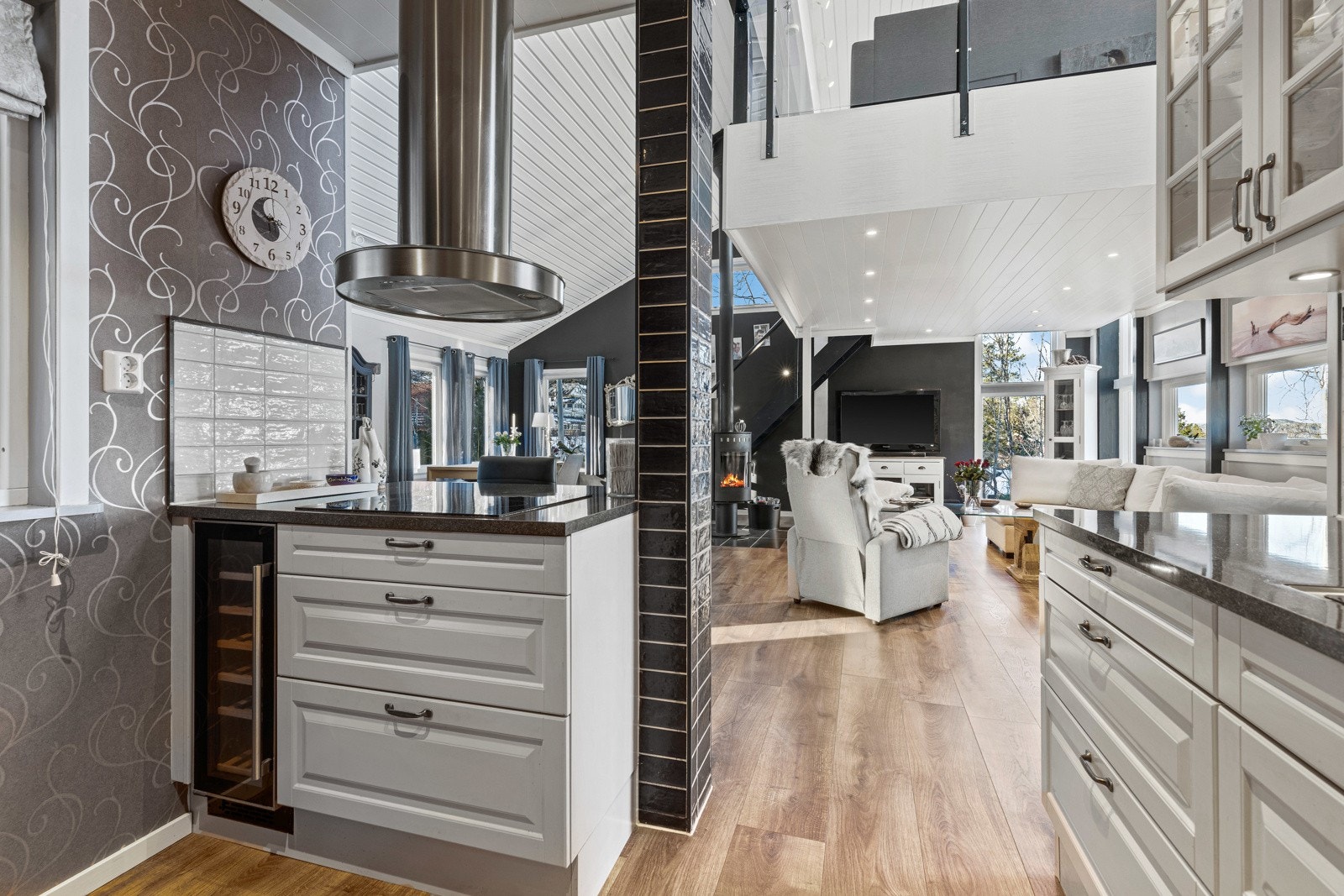 Mot stuen er det barløsning som skaper naturlig skille, og her er det plass til et par barstoler. Innredningen er takhøy og har profilerte fronter i lyse farger, noen høyskap med sortmalte fronter og vitrineskap. Galleribilde