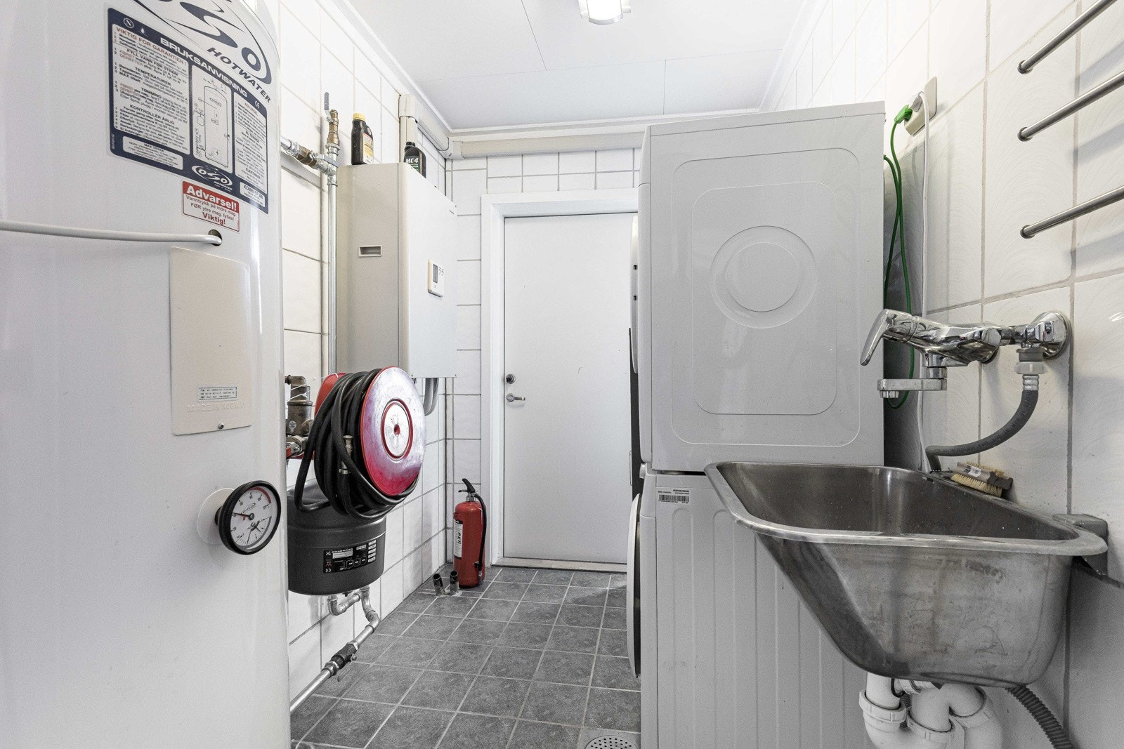 Vaskerommet har grå fliser på gulv og på veggene er det hvite og grå fliser. Rommet er utstyrt med utslagsvask av metall, opplegg for vaskemaskin, plass til tørketrommel, husbrannslange og ventilering. Galleribilde