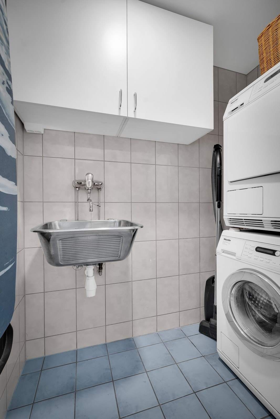 Praktisk, flislagt vaskerom med opplegg for vaskemaskin og tørketrommel. Rommet er også innredet med vask og et hyllesystem. Galleribilde