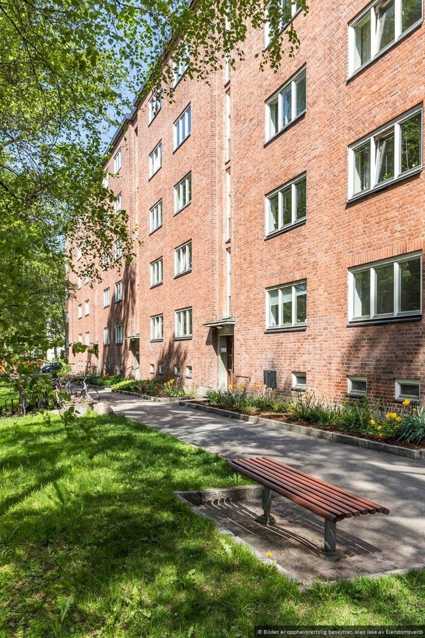 Den fine teglsteinsblokken er rammet inn av pent opparbeidede og beplantede grøntarealer. Galleribilde