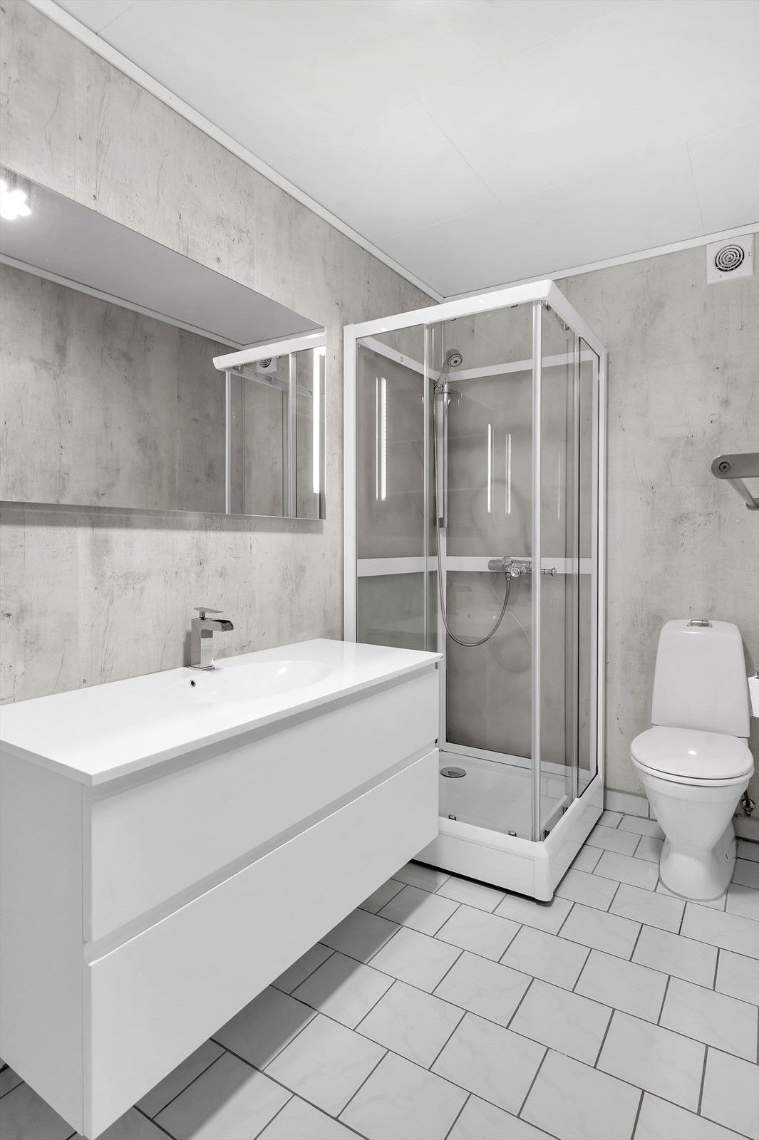 Badet har fliser på gulv og inneholder wc, nyere innredning samt dusjkabinett, vaskemasking og tørketrommel, og hyller langs veggen. Varmekabler i gulv. Galleribilde