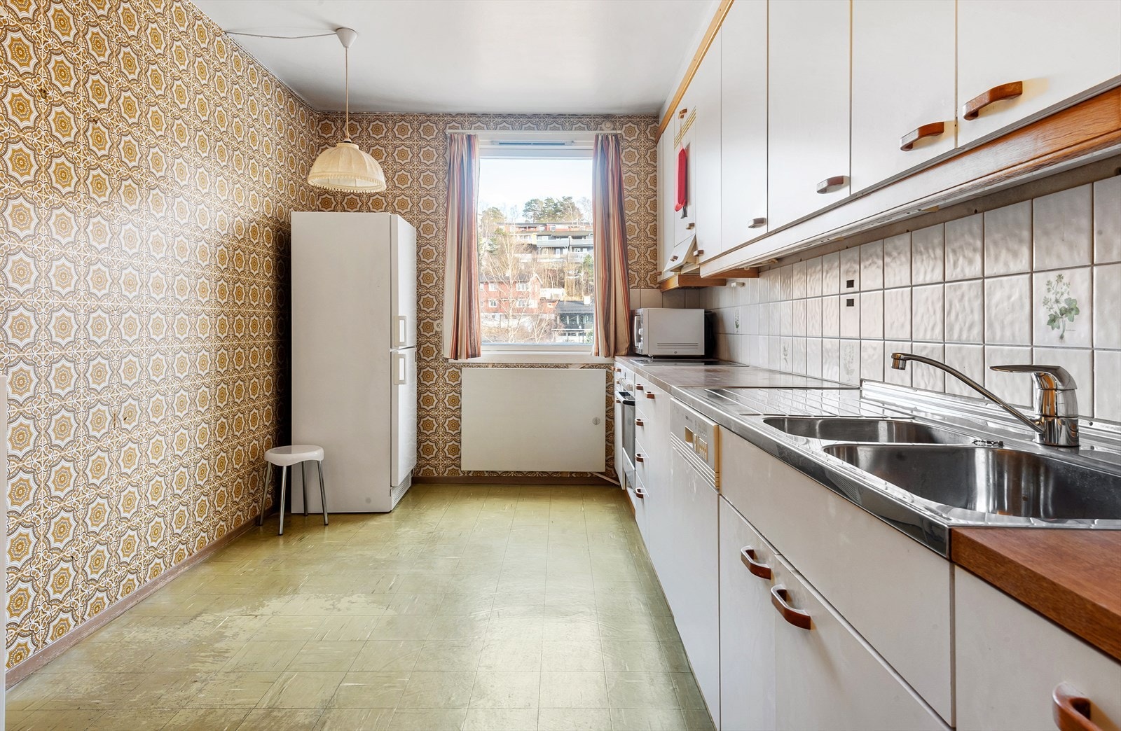 Romslig kjøkken med hvite glatte fronter, rustfritt stålbenkbeslag med vaskekum og skyllekum. Plass til spisegruppe. Galleribilde