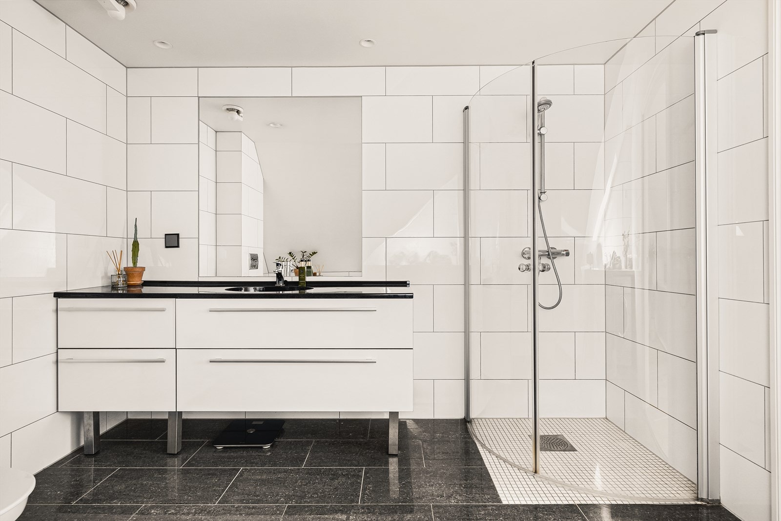 Badet er utstyrt med vegghengt toalett, helstøpt servant, skuffer under servant med slette fronter, innfelt speil og dusjdører i klart glass. Galleribilde