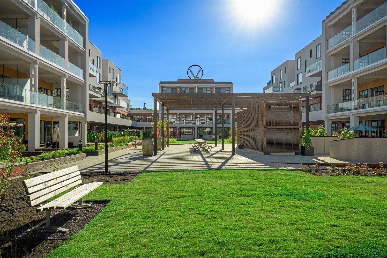 Pent opparbeidet bakgård med plen, plantekasser, benker, sittegrupper og pergola med langbord. Galleribilde