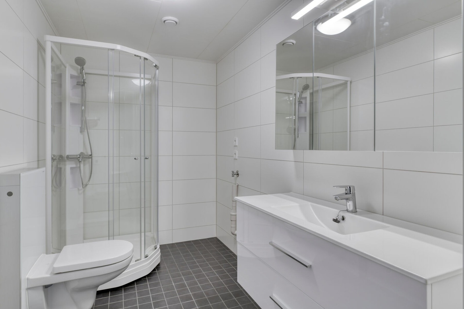 Badet har dusj, toalett, innredning med servant, skuffer, speilskap og lys, samt opplegg for vaskemaskin/tørketrommel Galleribilde