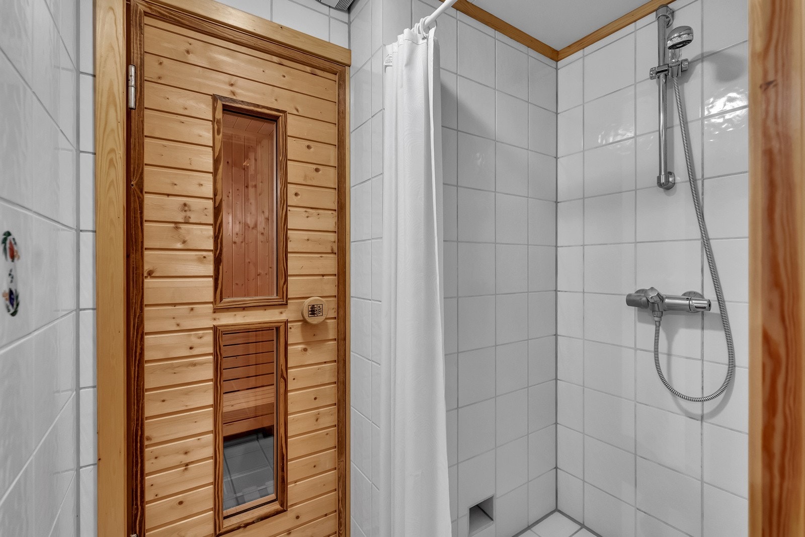 I kjelleren er det et velholdt og pent dusjrom med tilliggende badstue. Dusjrommet har hvite fliser på veggene og matchende fliser på gulv med gulvvarme, og i en nisje er det montert dusjarmatur Galleribilde