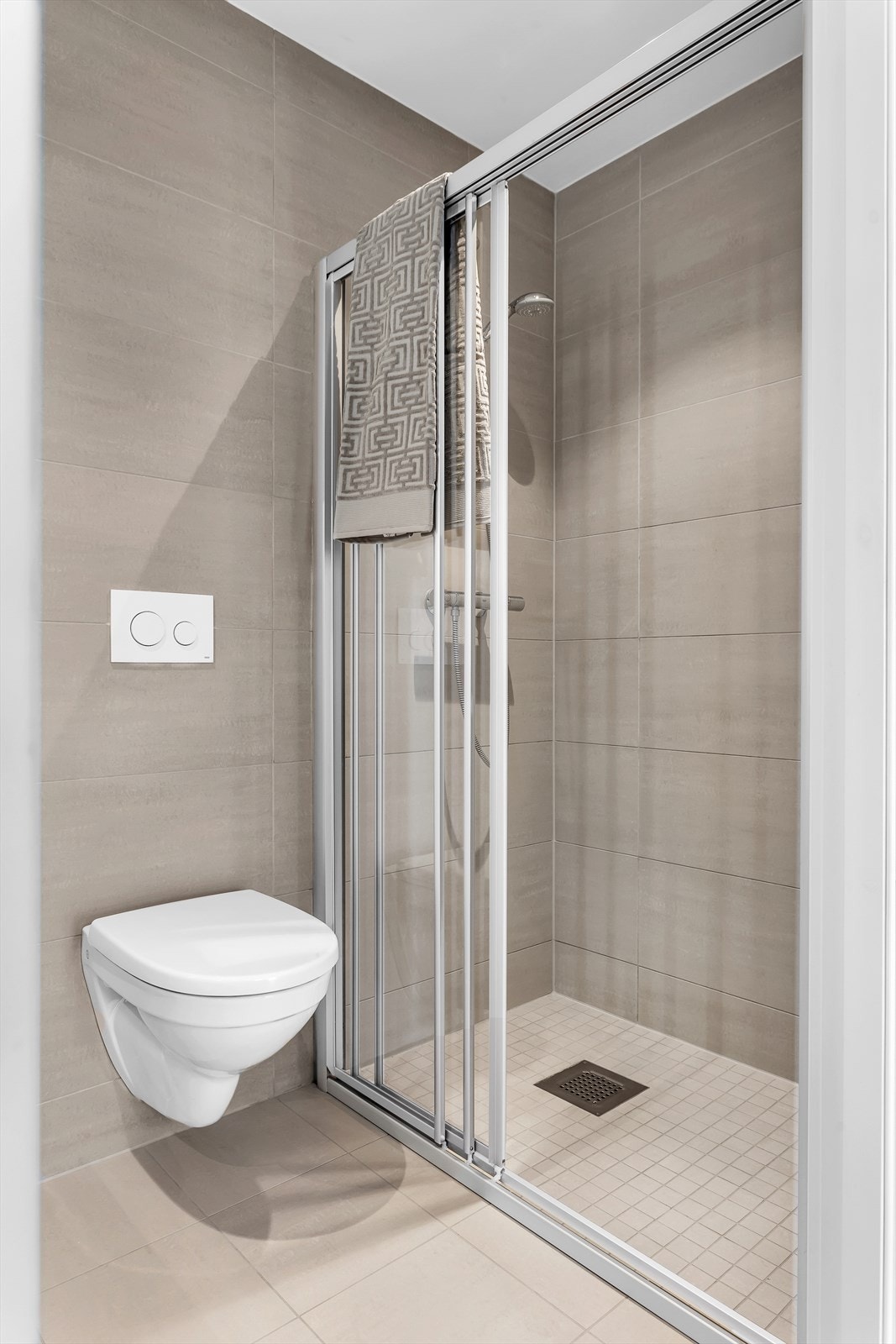 Flislagt baderom med vegghengt klosett og dusj med dusjvegger i herdet glass Galleribilde