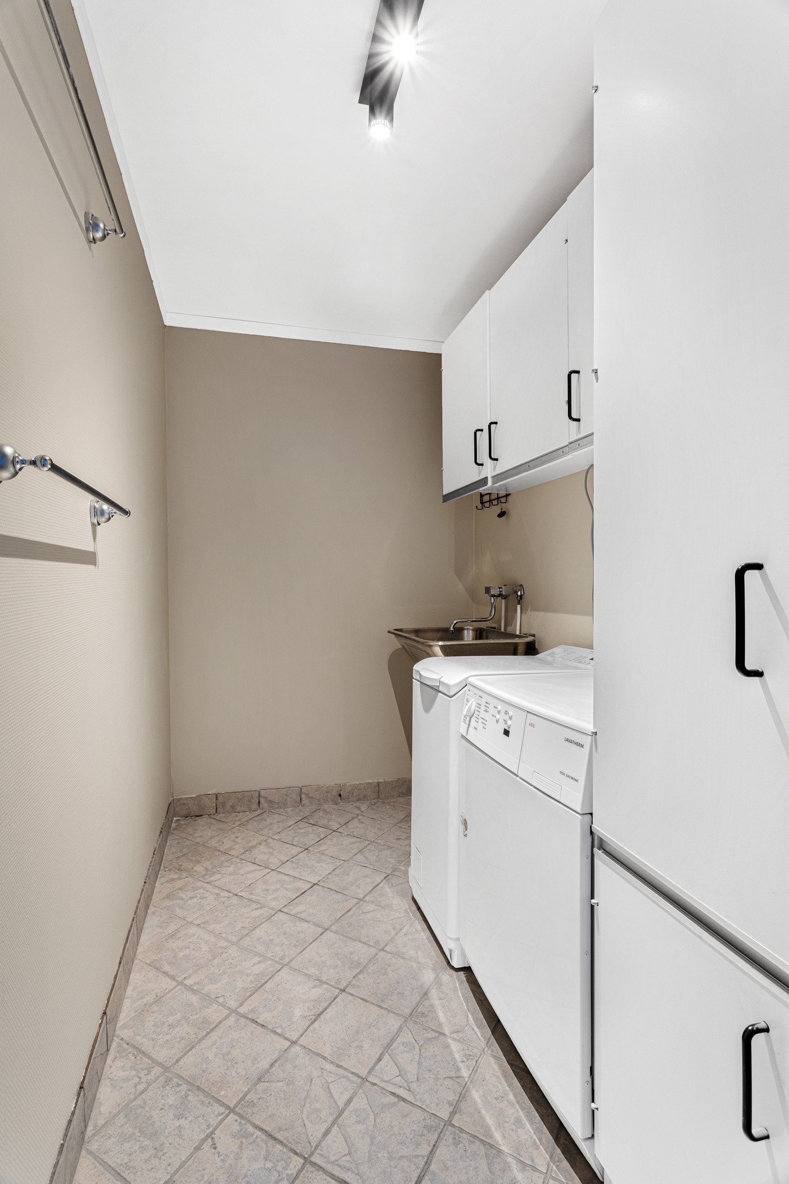 Praktisk separat vaskerom med flis på gulv, sokkelflis, og glatte, malte vegger. Galleribilde