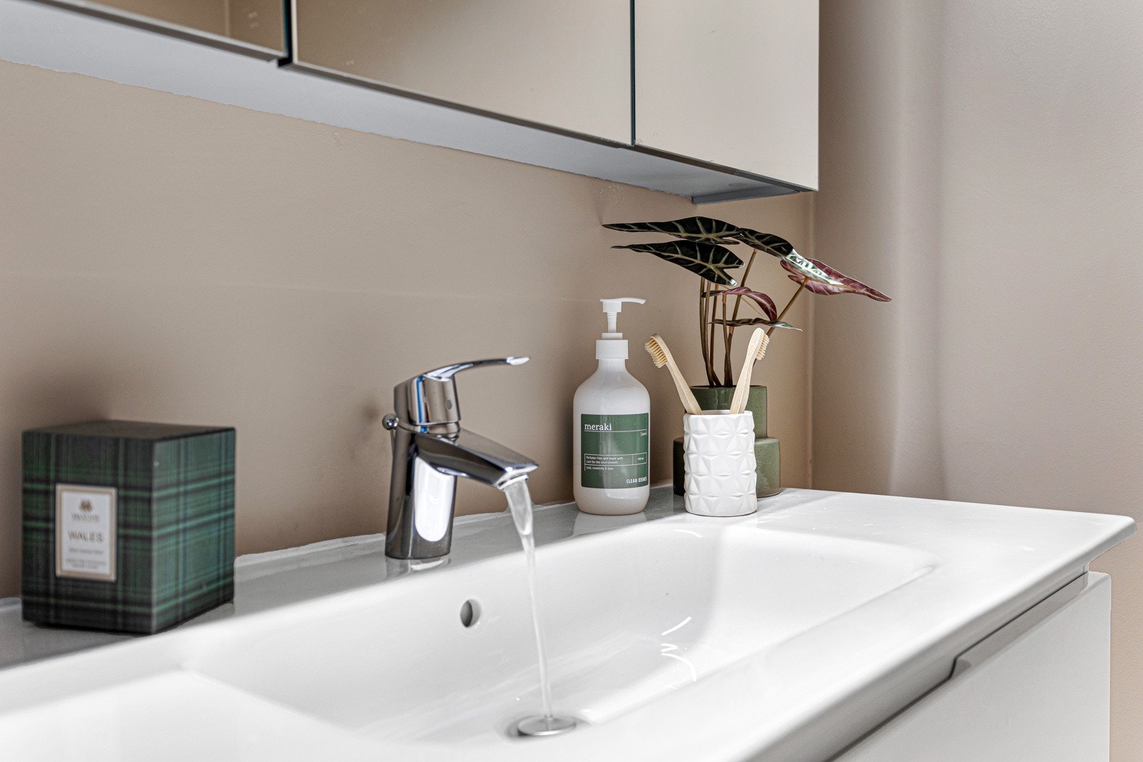 Rommet har moderne innredning med hvite, glatte skuffefronter, heldekkende servant og stort speilskap med tre dører og stilig belysning. Galleribilde