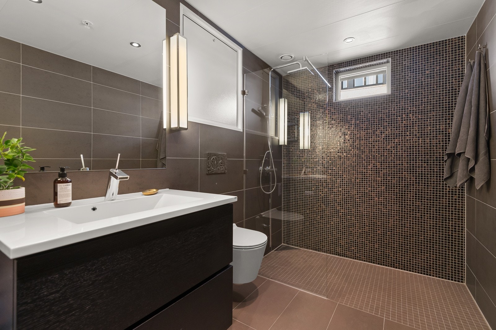 Flislagt baderom fra byggeår med gulvvarme, opplegg for vaskemaskin og nedsenket himling med downlights Galleribilde