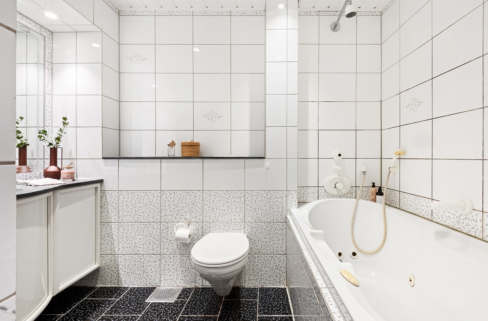 Bad/wc med innmurt og flislagt badekar, vegghengt toalett og servant med innmurt speil. Galleribilde