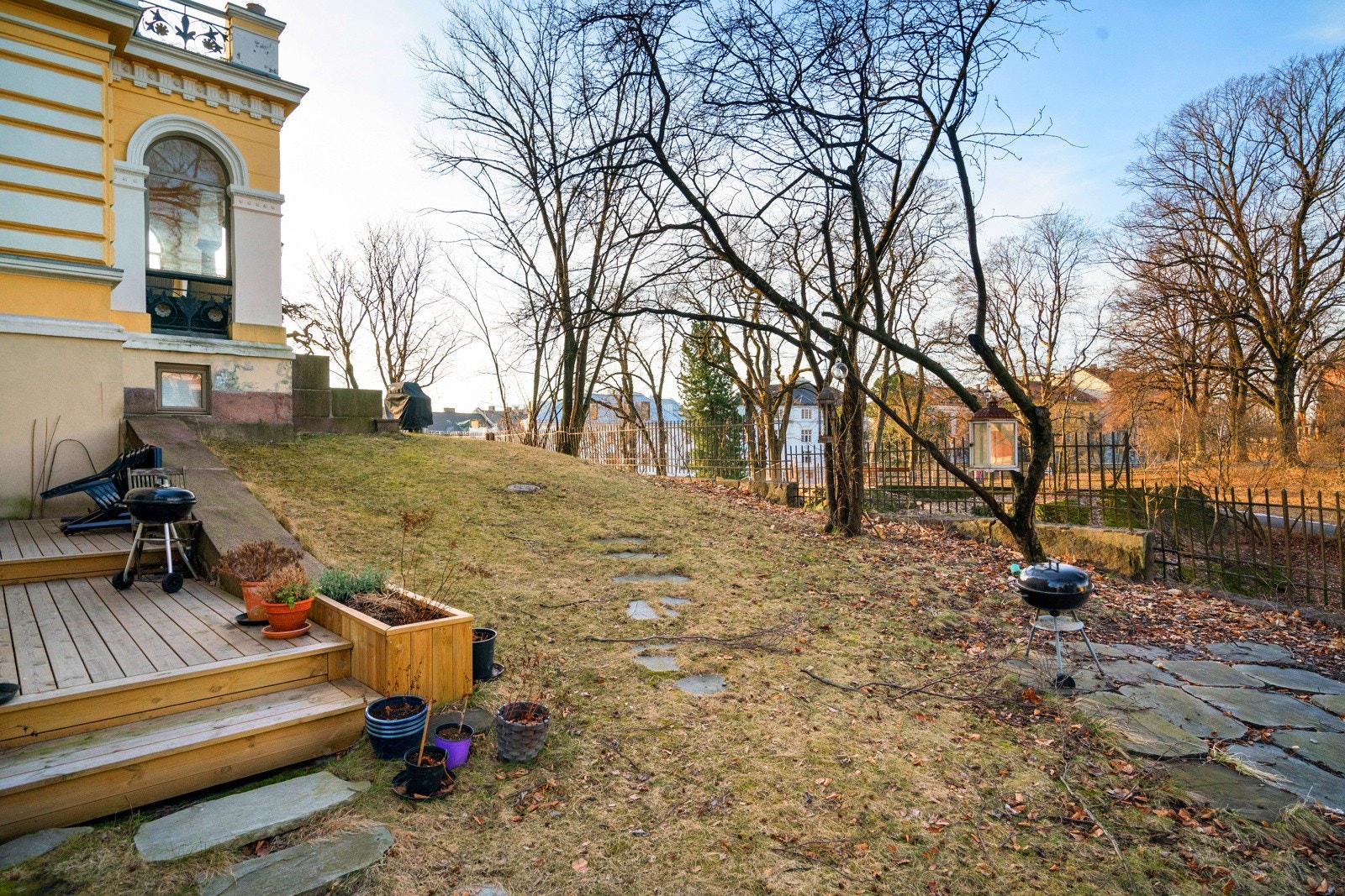 Rundt villaen er det en idyllisk hage med grønne plener, prydbusker og store trær. Det hele innrammes av sortmalte smijernsgjerder. Galleribilde