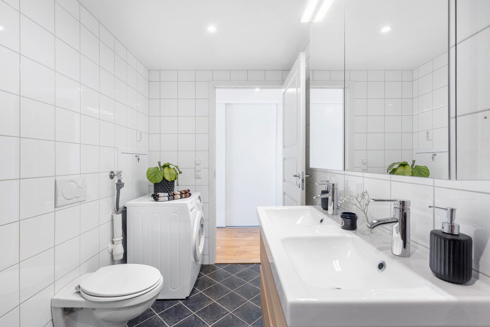 Pent flislagt bad med dobbeltservant med speilskap og underskap. Veggmontert WC, dusjhjørne, kran og avløp for vaskemaskin. Galleribilde