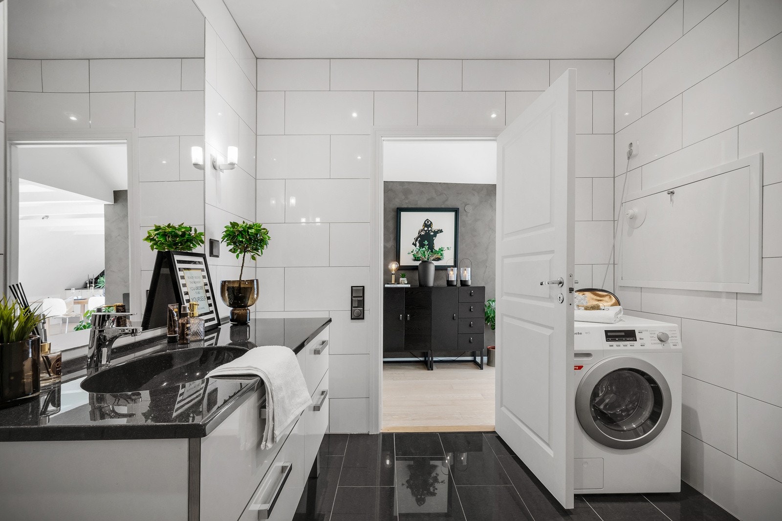 Badet inneholder benkeskap med servant, vegghengt toalett, dusjdører og opplegg for vaskemaskin Galleribilde