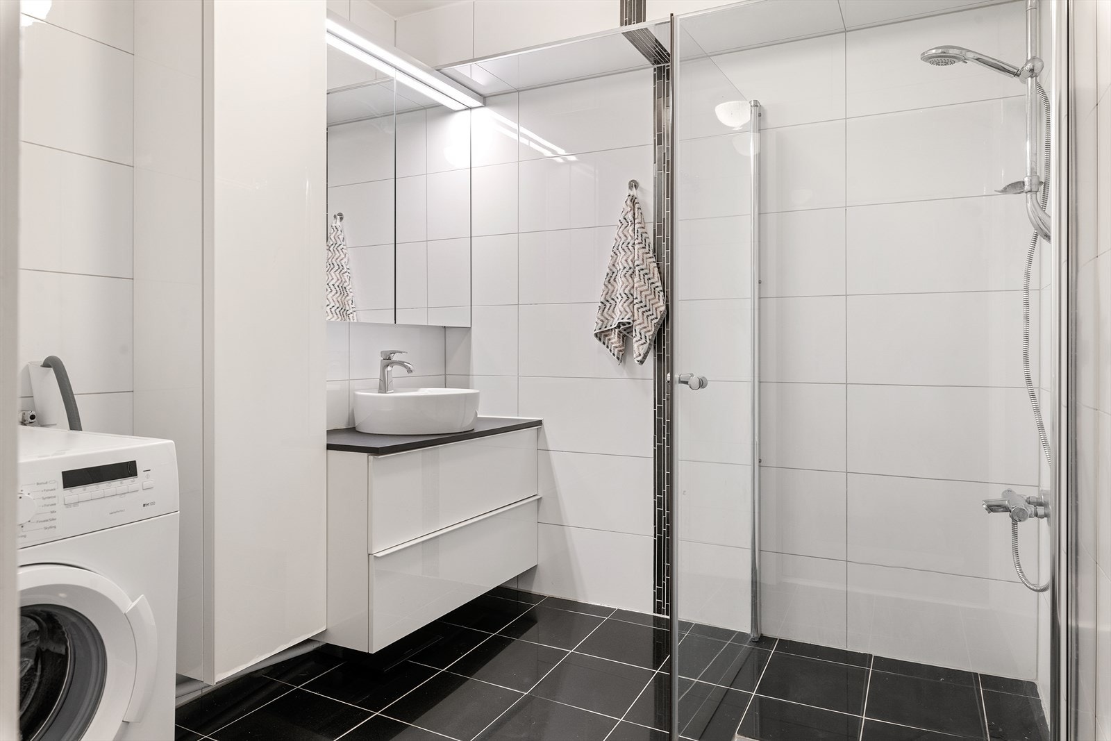Leiligheten har et flislagt baderom fra 2013 med varmekabler. Badet har dusjdører i herdet glass, speilskap med overliggende belysning, opplegg for vaskemaskin, baderomsinnredning med høyglans fronter og heldekkende servant. Galleribilde