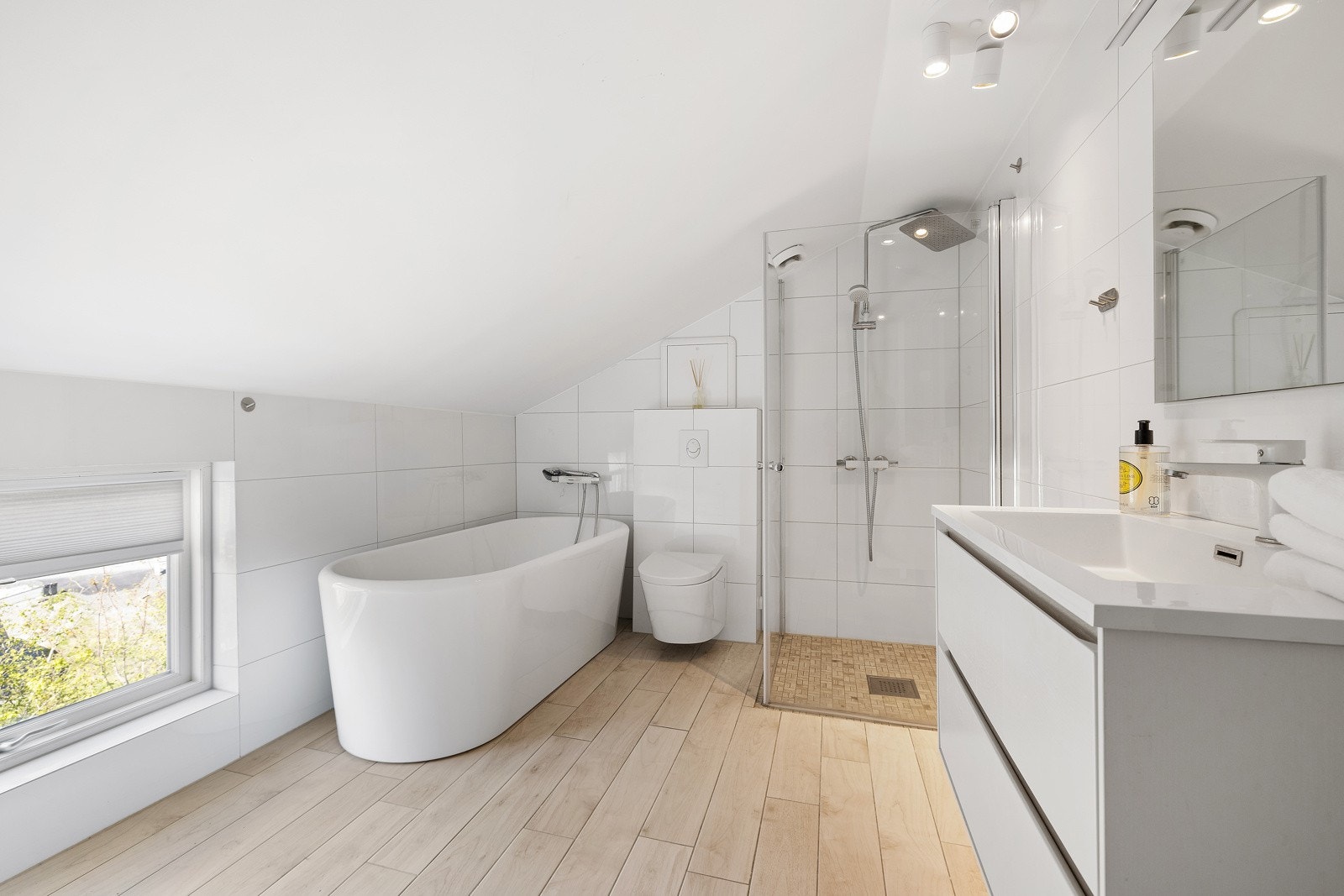 Delikat, flislagt baderom i andre etasje innredet med dusjnisje med regnfallsdusj, servant med skuffeseksjon, vegghengt klosett og badekar. Galleribilde