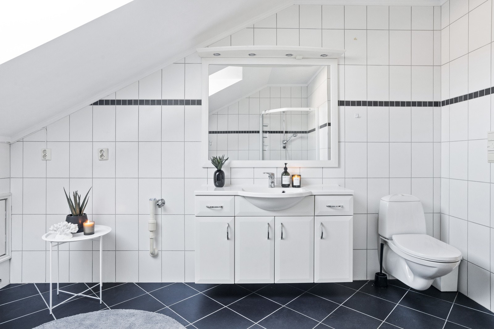 Baderommet inneholder servant med underskap, speil med overlys, vegghengt toalett og dusjnisje med glassdører. Galleribilde