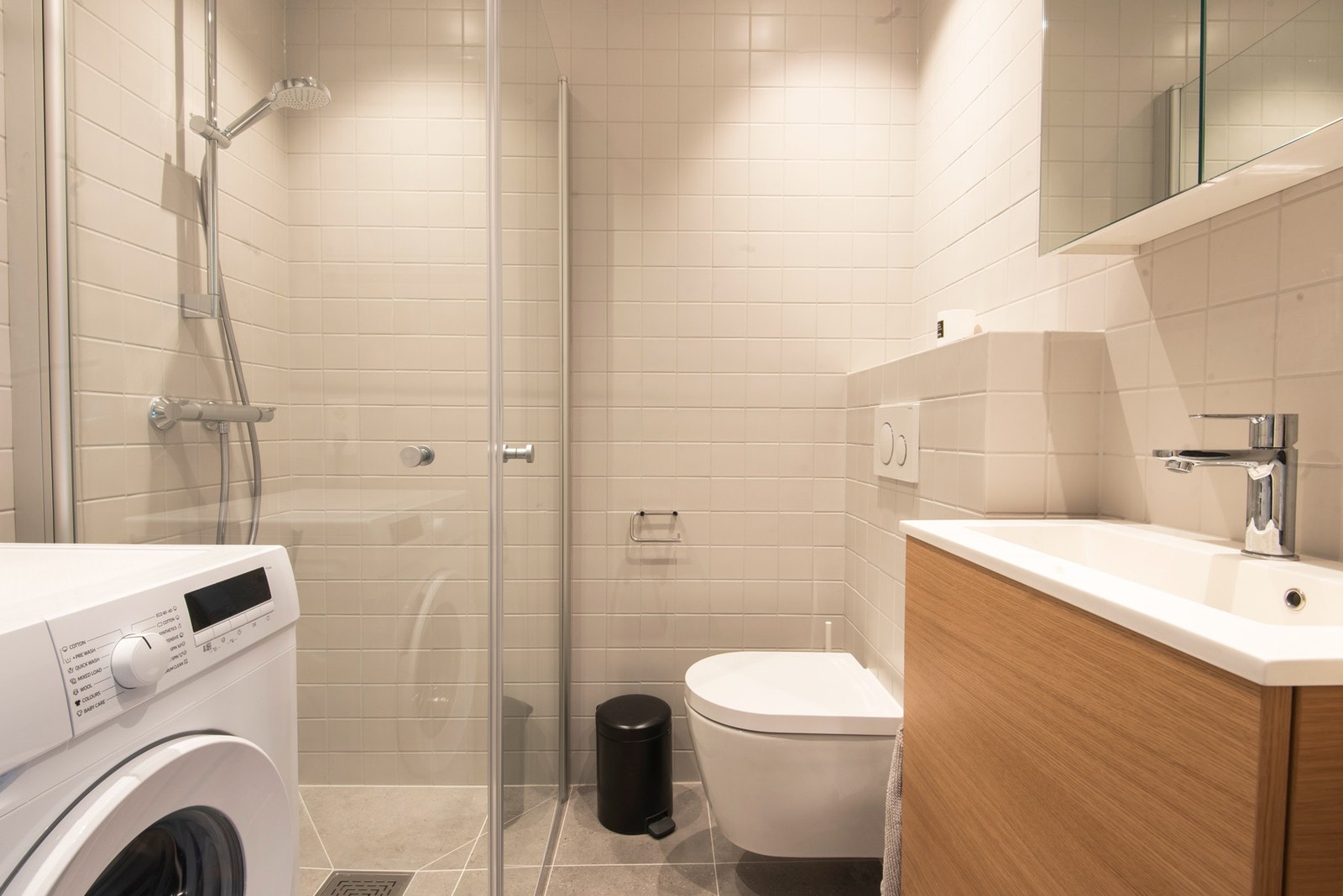 Bad med romslig dusj, vegghengt toalett, vaskemaskin og servantskap. Dusjdører kan felles helt inn når de ikke er i bruk Galleribilde