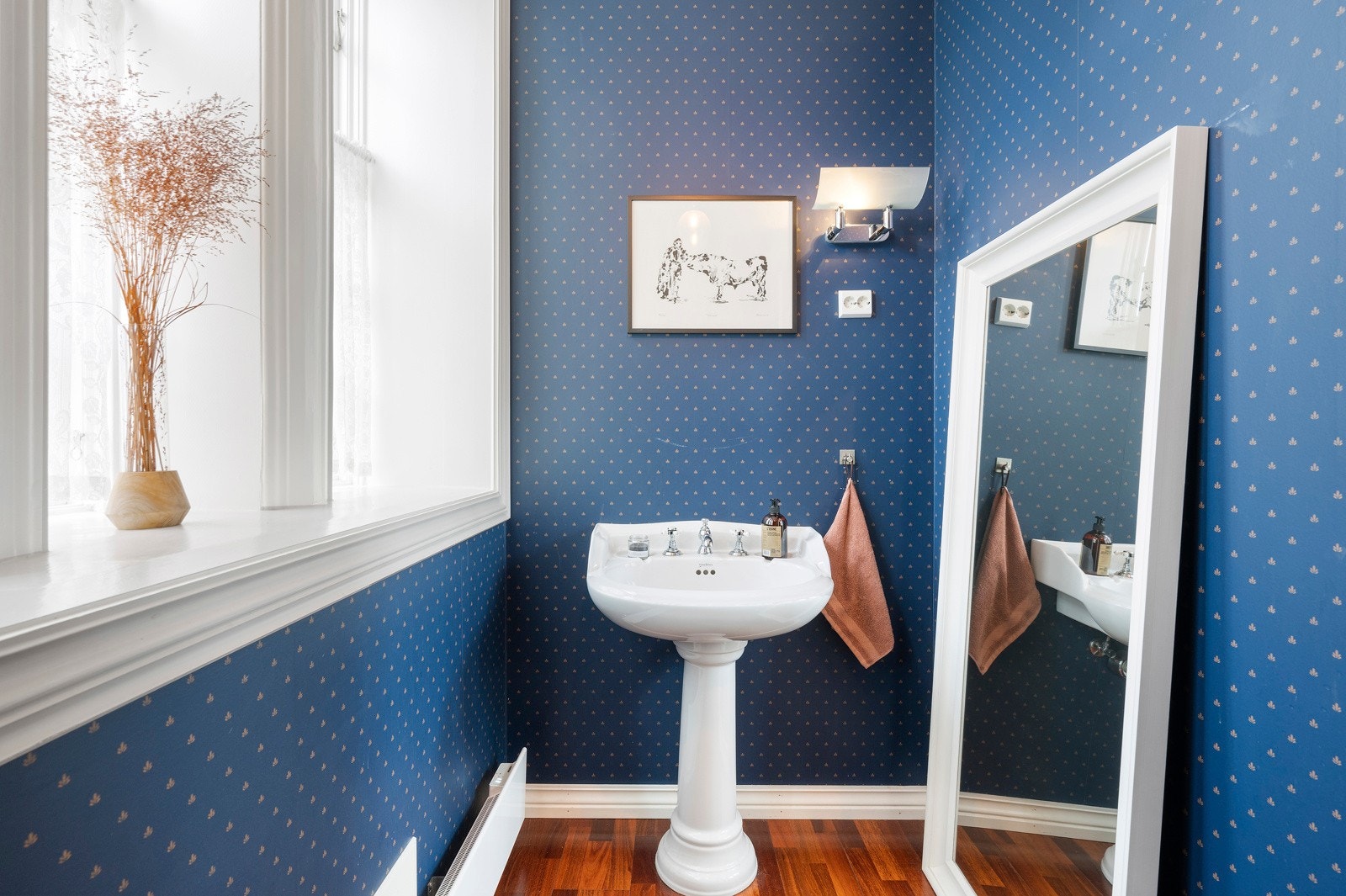 Toalettrommet har trestavs parkett, stort vindu og blå tapet på veggene. Galleribilde