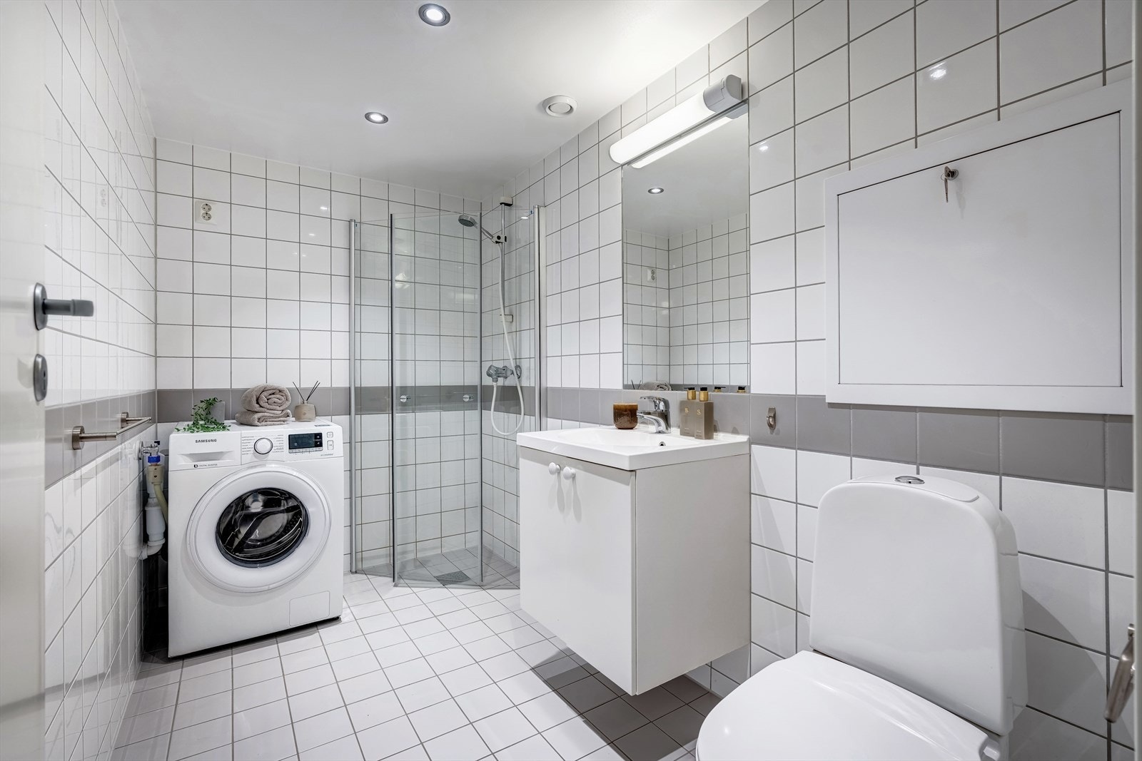 Lekkert bad med dusj med innfellbare dører i herdet glass, servant i helstøpt plate, wc og speil. Galleribilde