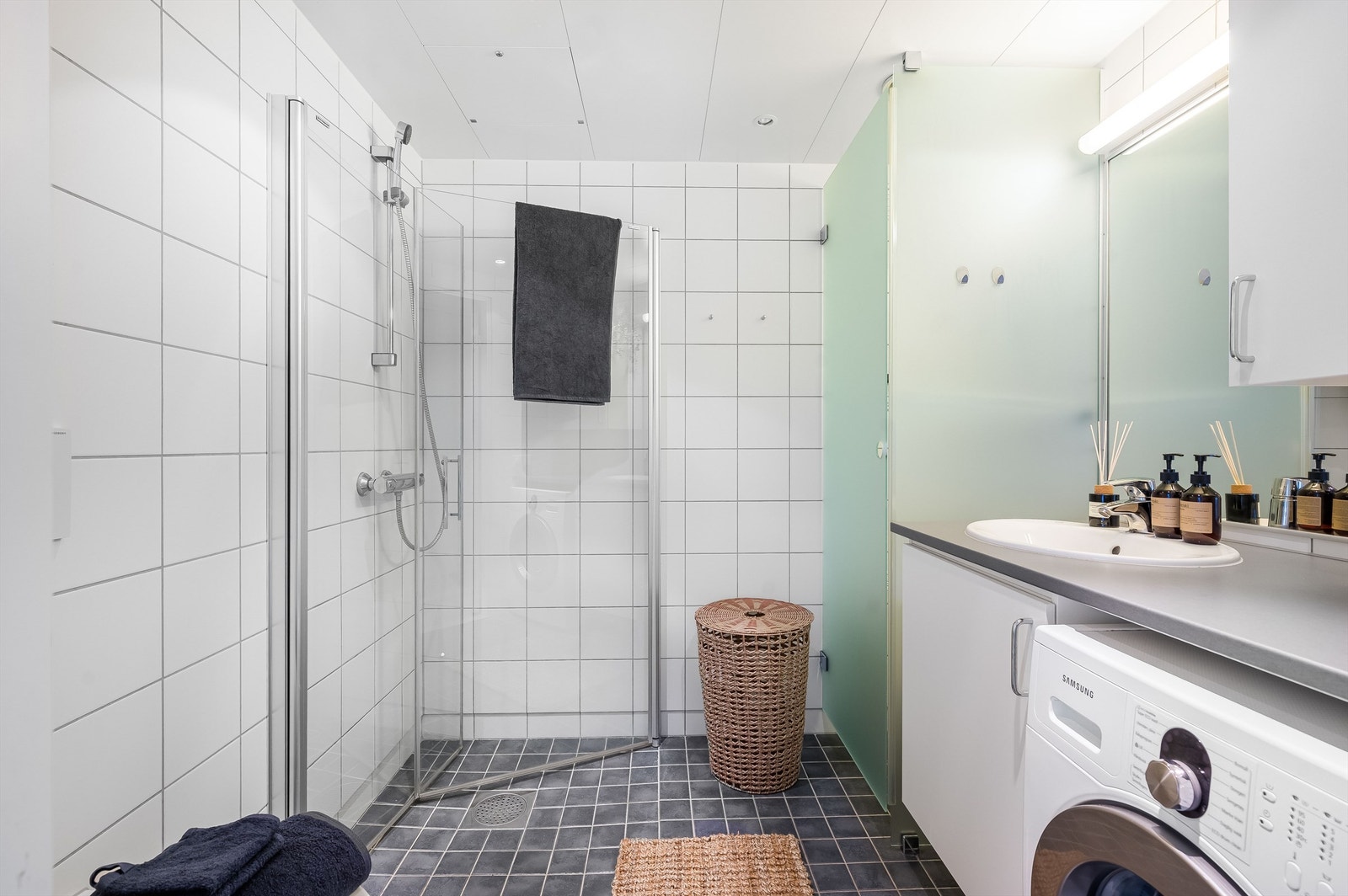 Innbydende og meget romslig bad med hvite fliser på vegg, gråmelerte fliser med varme i gulv og downlights i himling Galleribilde