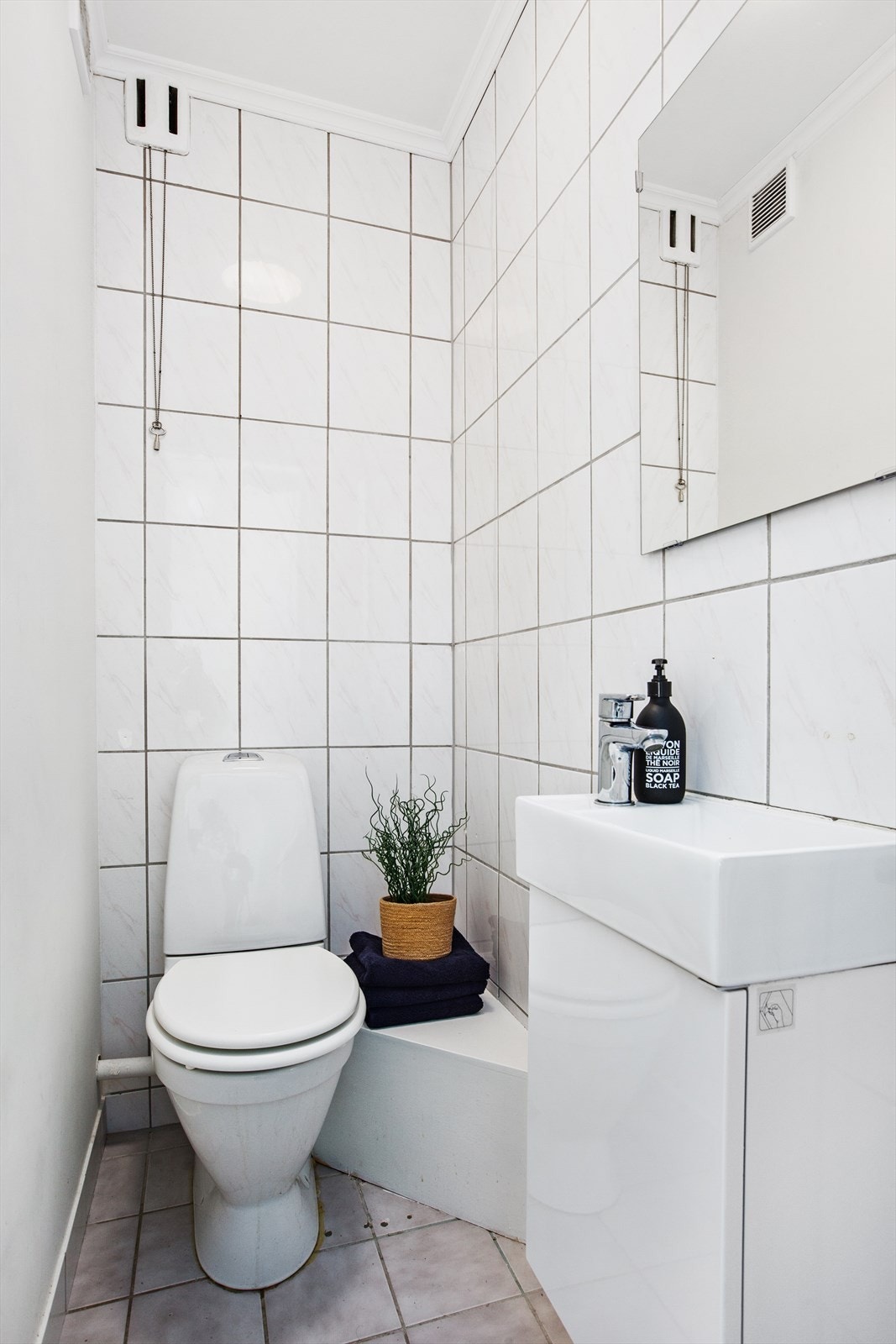 Separat WC med fliser på gulv og vegger. Innredningen består av servantskap med servant og ett-greps blandebatteri, speil over servant og toalett. Galleribilde