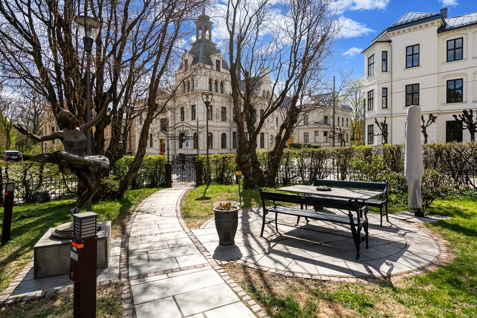 Tomtegrunnen er avgrenset med gjerde og flott opparbeidet med plen, beplantning, brostein, trær og skulptur. Det er adkomst via nydelig smijernsport med rik utsmykning. Galleribilde
