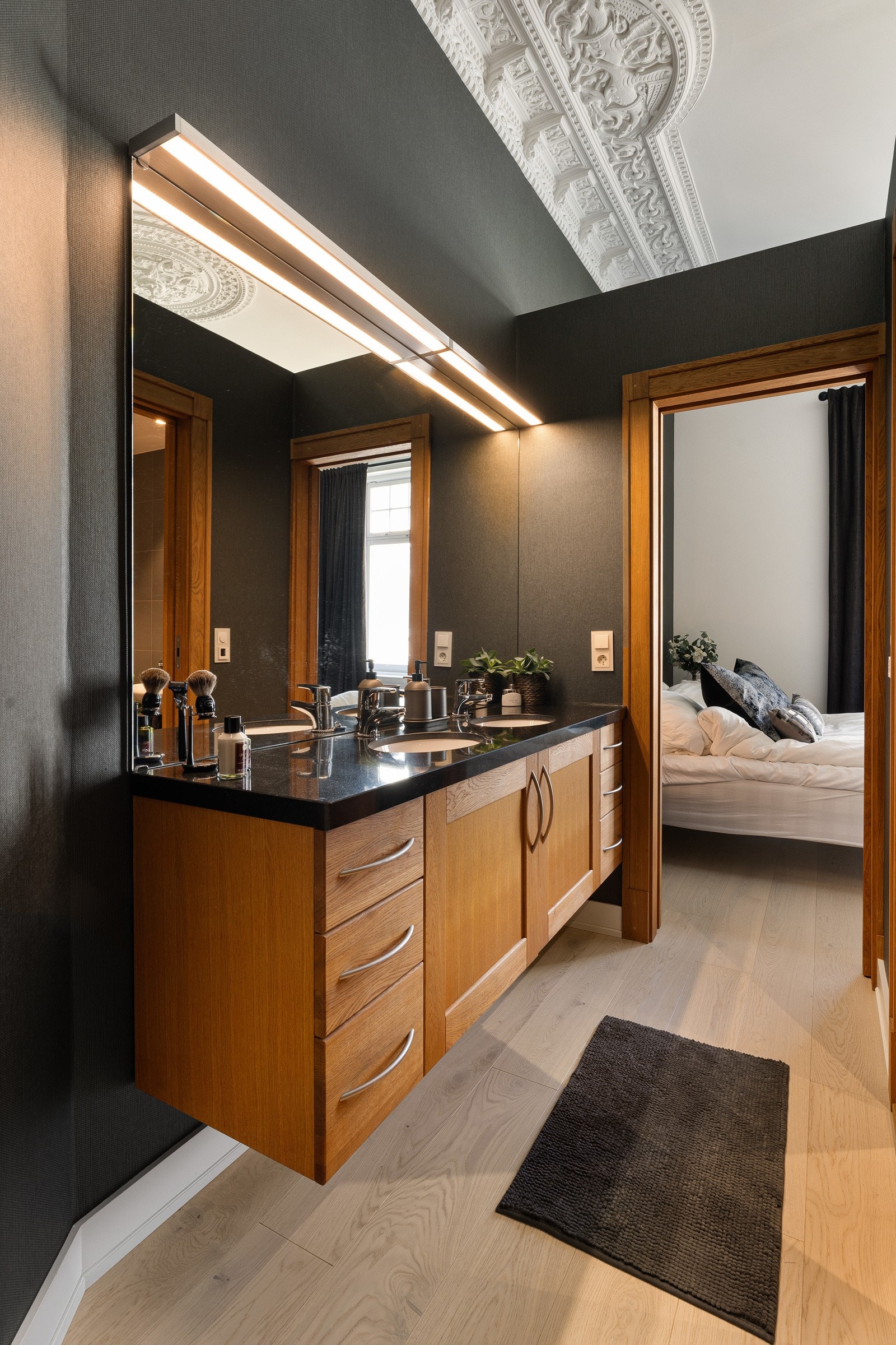 Det ene badet har adkomst fra soverommet via et rom med dobbel servantinnredning - en smart, tidseffektiv løsning. Skapinnredningen har rammefronter i heltre eik og benkeplate i sort granitt med to underlimte ovale, hvite servanter. Galleribilde