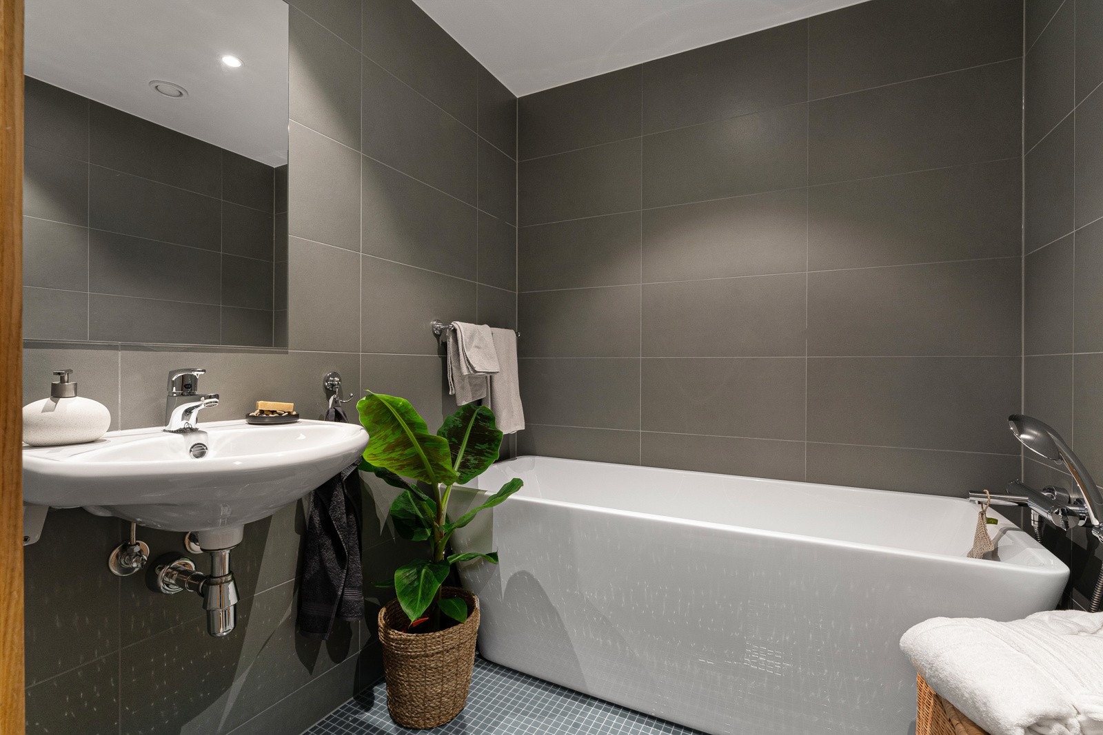 Badet har mosaikkfliser på gulvet og grå, store fliser på veggene. Galleribilde