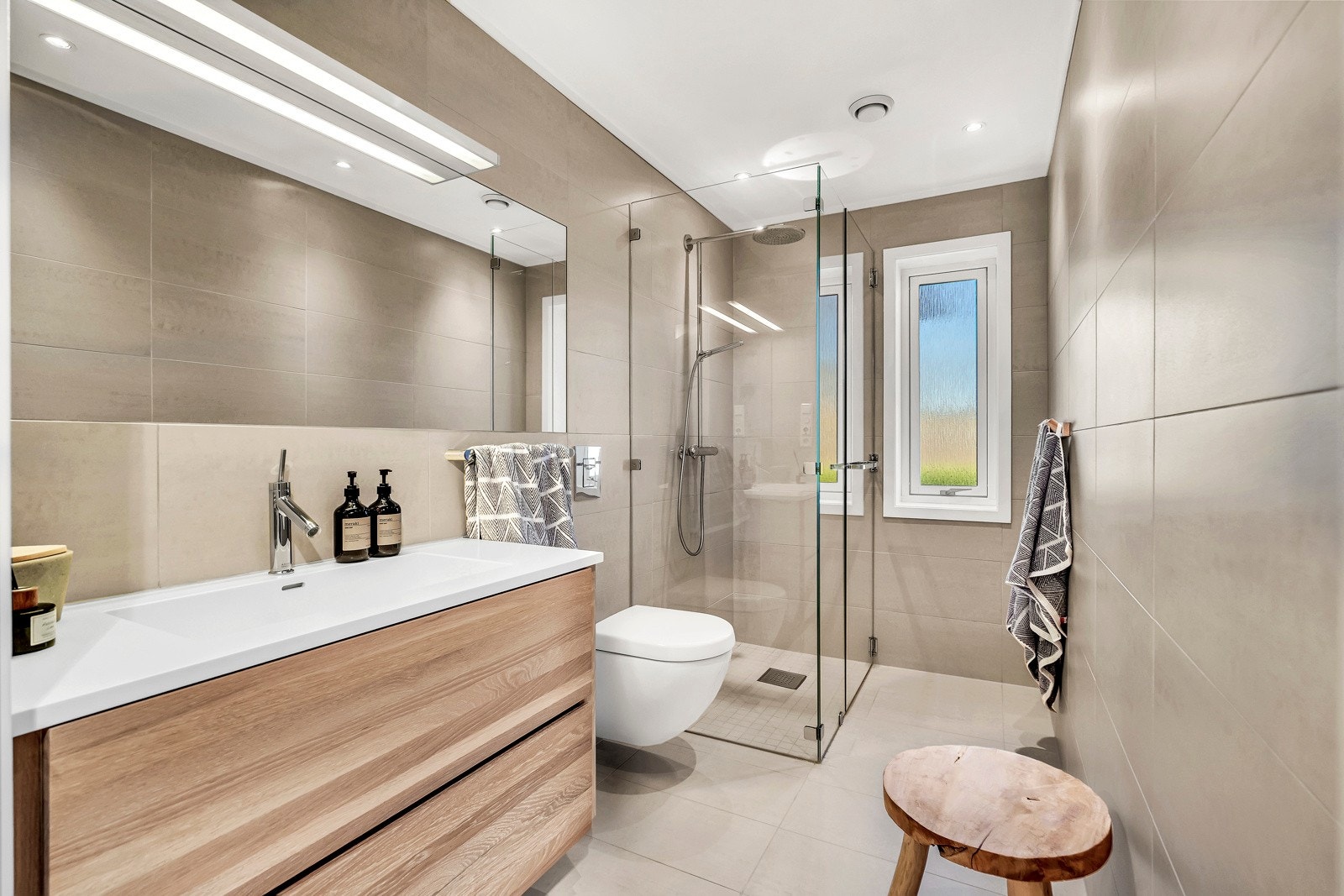 Flislagt bad med eksklusiv innredning. Innredning i heltre eik med Corian benkeplate. Speiallaget dusjvegger i ekstra tykt, herdet glass. Hansgrohe Axor armatur og Villeroy & Boch wc. Galleribilde