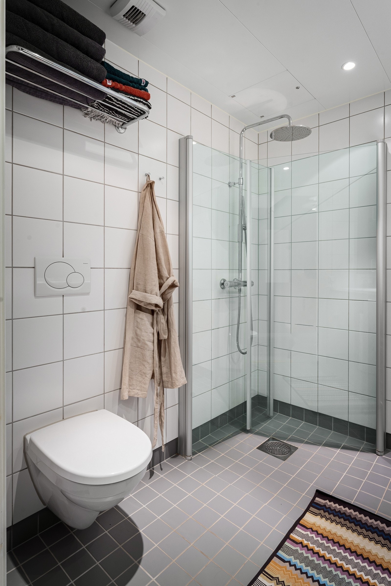 Under benken, på hver side av benkeskapet, er det opplegg for vaskemaskin og mulighet for tørketrommel. Bakenfor rette, innfellbare dører i herdet glass er det dusjhjørne med både hånddusj og regnfallsdusj. Vegghengt toalett. Galleribilde