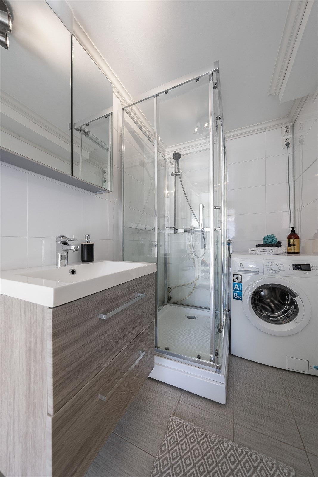 Badet inneholder vegghengt toalett, dusjkabinett og servantinnredning med slette fronter og overskap med speildører. Det er opplegg for vaskemaskin Galleribilde