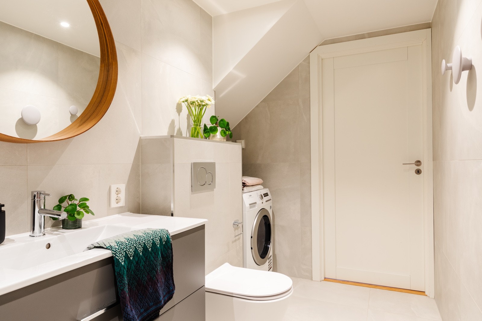 Badet er smakfullt innredet med servantskap, speil, veggmontert WC og lyse fliser. Opplegg til vaskemaskin. Galleribilde