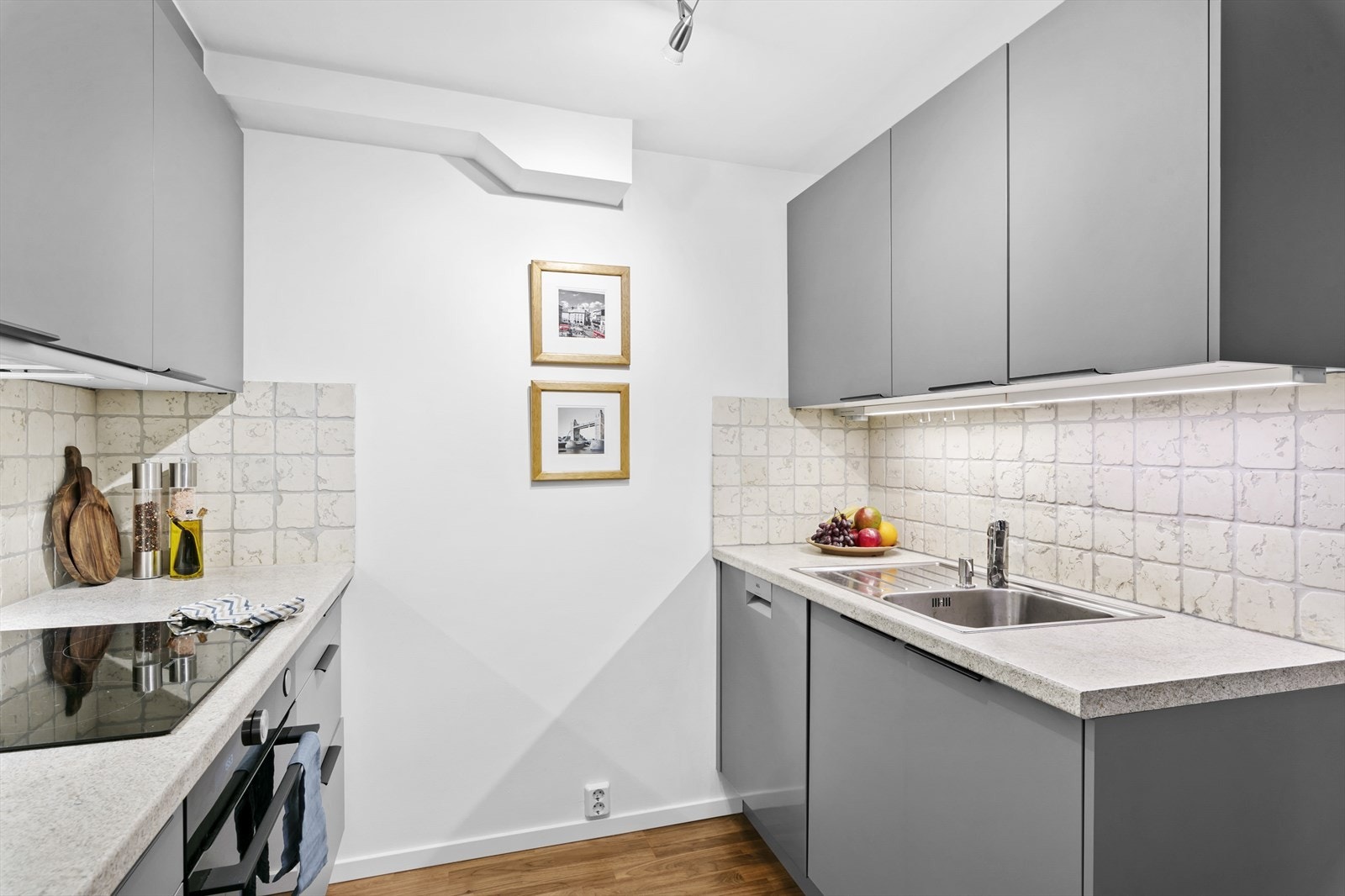 Kjøkkeninnredning med glatte fronter, laminert benkeplate og flisfelt over. Lys under overskap. Galleribilde