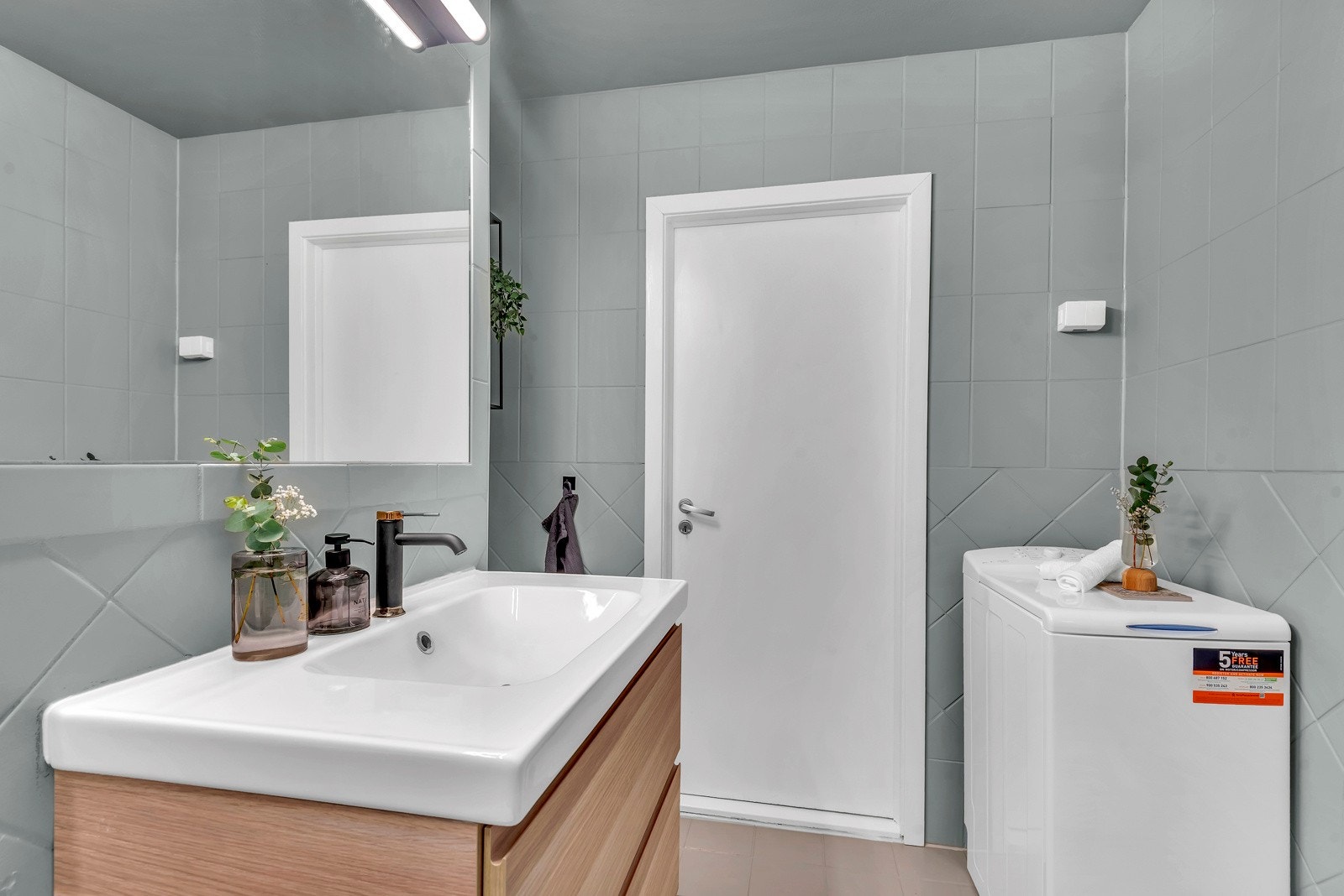 Delkat bad med opplegg for vaskemaskin. Det er fliser på vegger og gulv Galleribilde