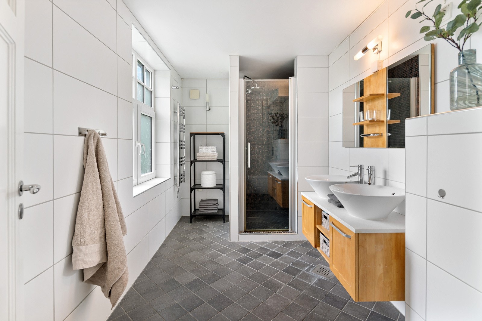 Boligen har to flotte bad og et praktisk vaskerom. Alle rommene er fra 2008 og badet i første etasje har adkomst fra entreen. Badet har mørkegrå gulvfliser i 15 x 15 cm og hvite veggfliser i 30 x 60 cm. Det er varme i gulvet og innfelte downlights. Galleribilde