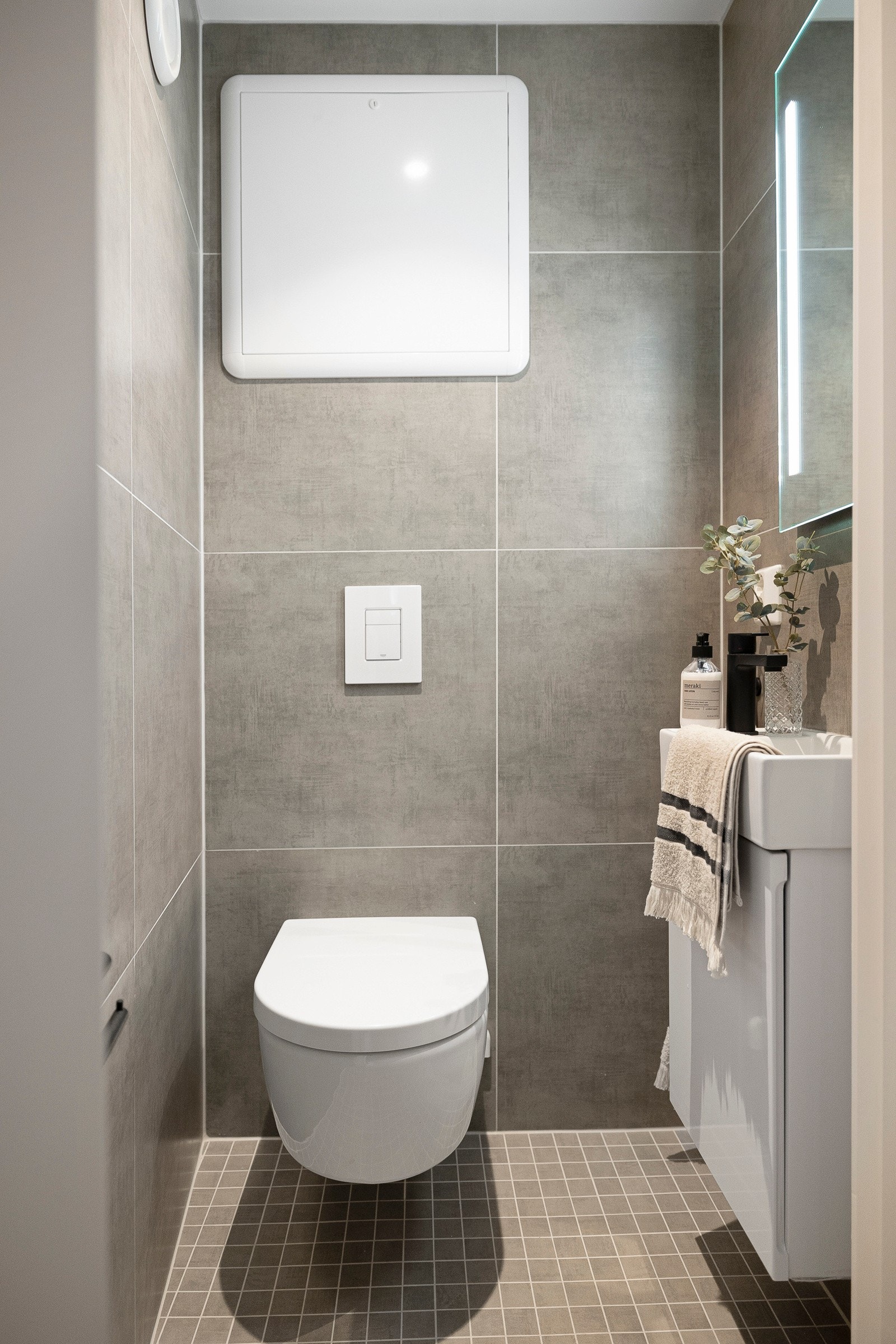 Vegg-i-vegg med badet er det et pent, separat wc-rom med store, grå fliser på veggene og matchende fliser på gulv med gulvvarme. Galleribilde