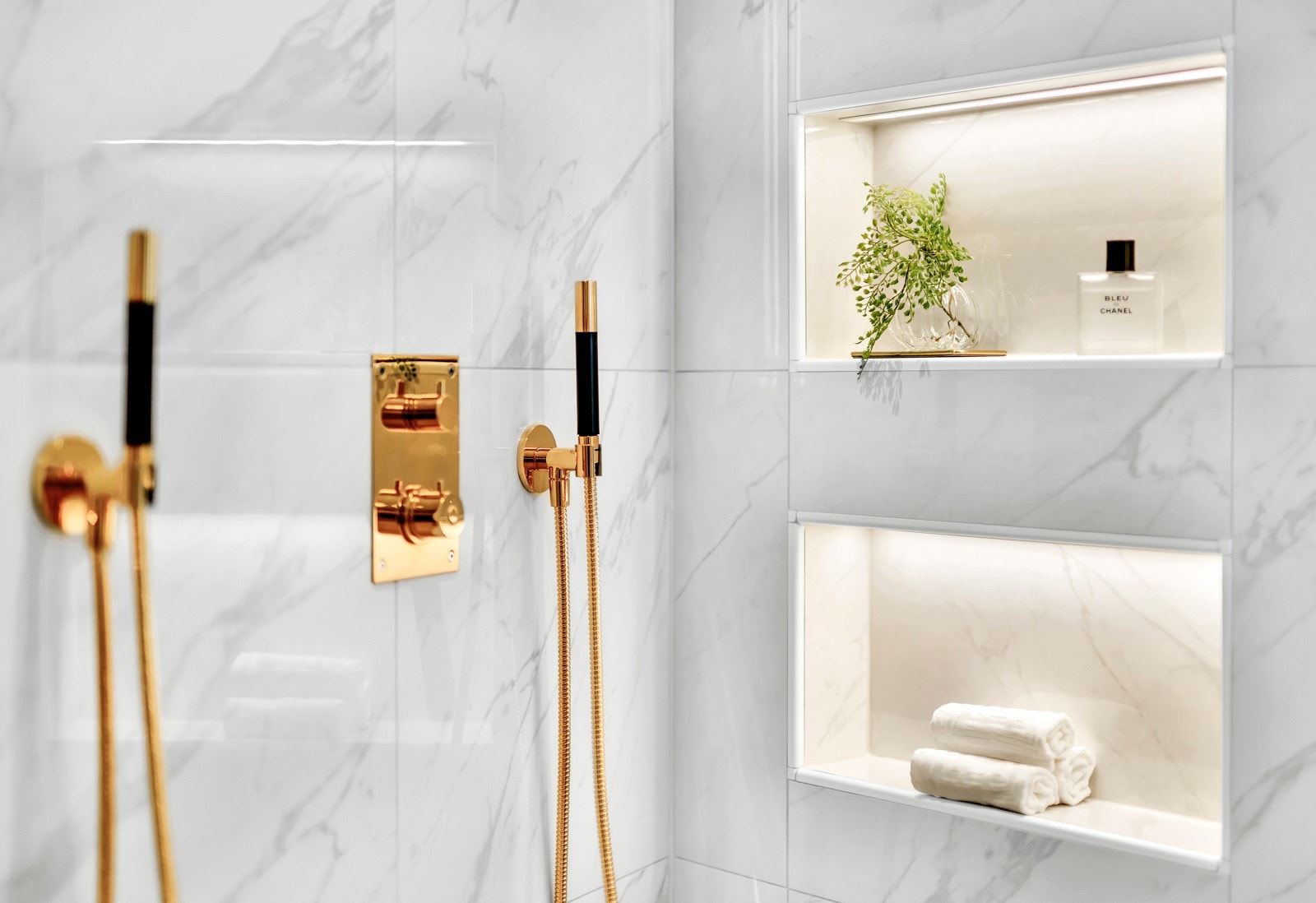 Gullfarget armatur i lekker kontrast til marmor, og to takmonterte regnfallsdusjer troner over en bred dusjnisje. Galleribilde