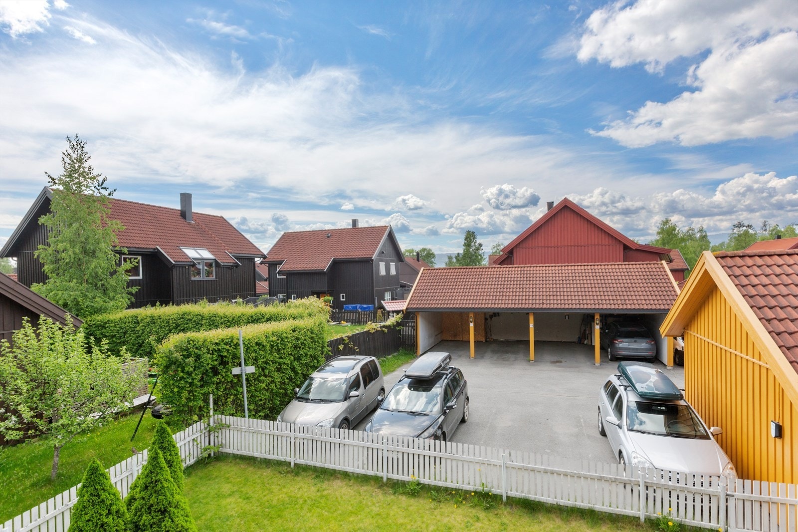 Asfaltert innkjøring og gårdsplass med oppmerkede parkeringsplasser og carporter. Galleribilde