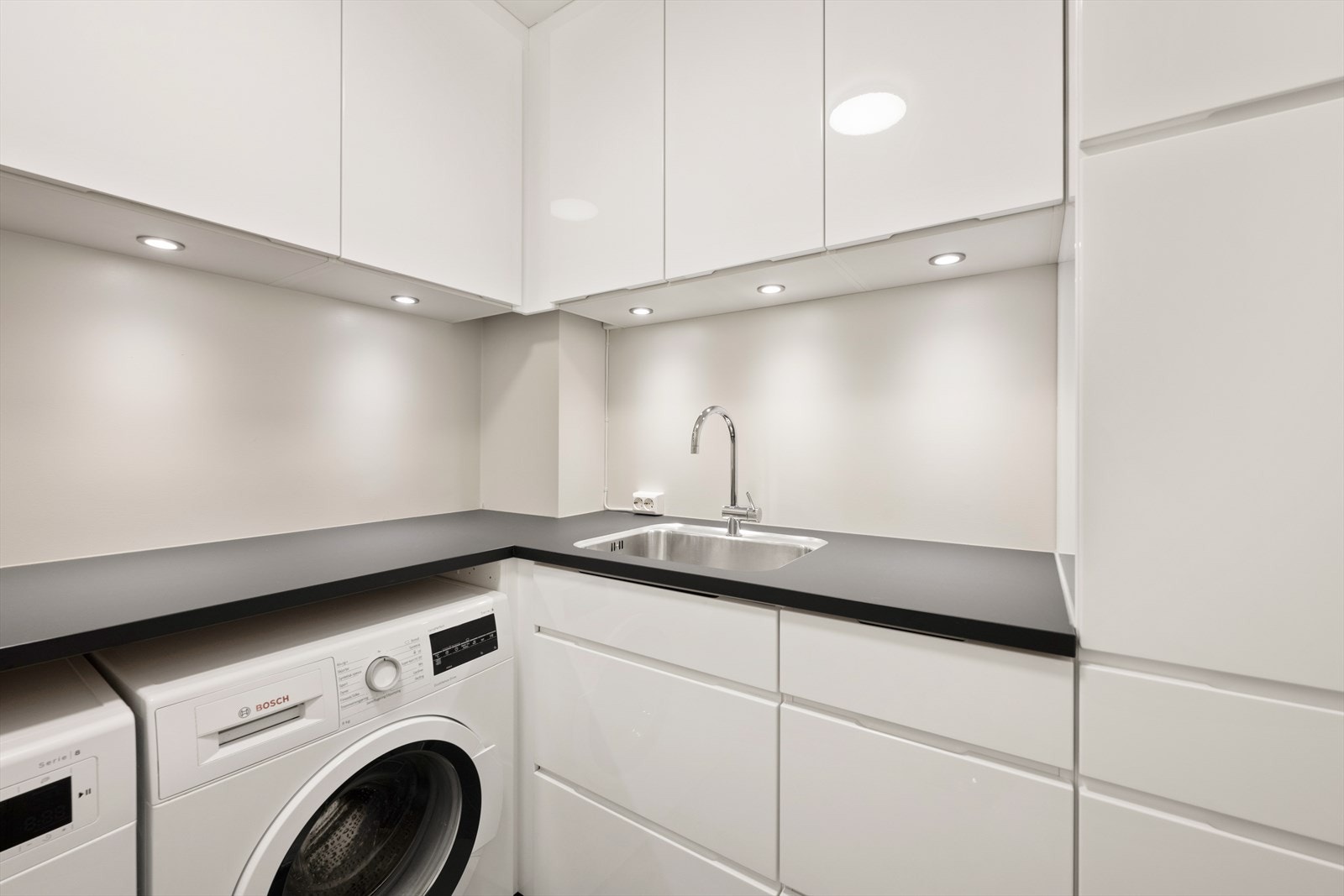 Separat vaskerom med mye skapplass, benkeplate med utslagsvask og opplegg for vaskemaskin. Galleribilde