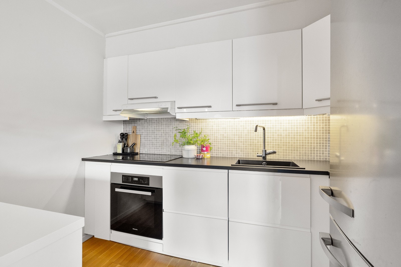 Lys innredning med glatte, folierte fronter og laminat benkeplate med nedfelt kum i svart kvartskompositt. Galleribilde