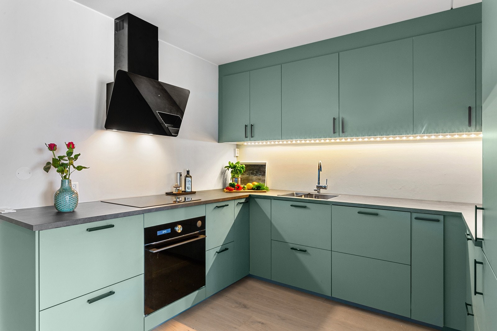 Kjøkkenet fra 2021 er lekkert med fronter i dyp mintfarge, benkeplate i grå laminat og alle hvitevarer integrert. Galleribilde