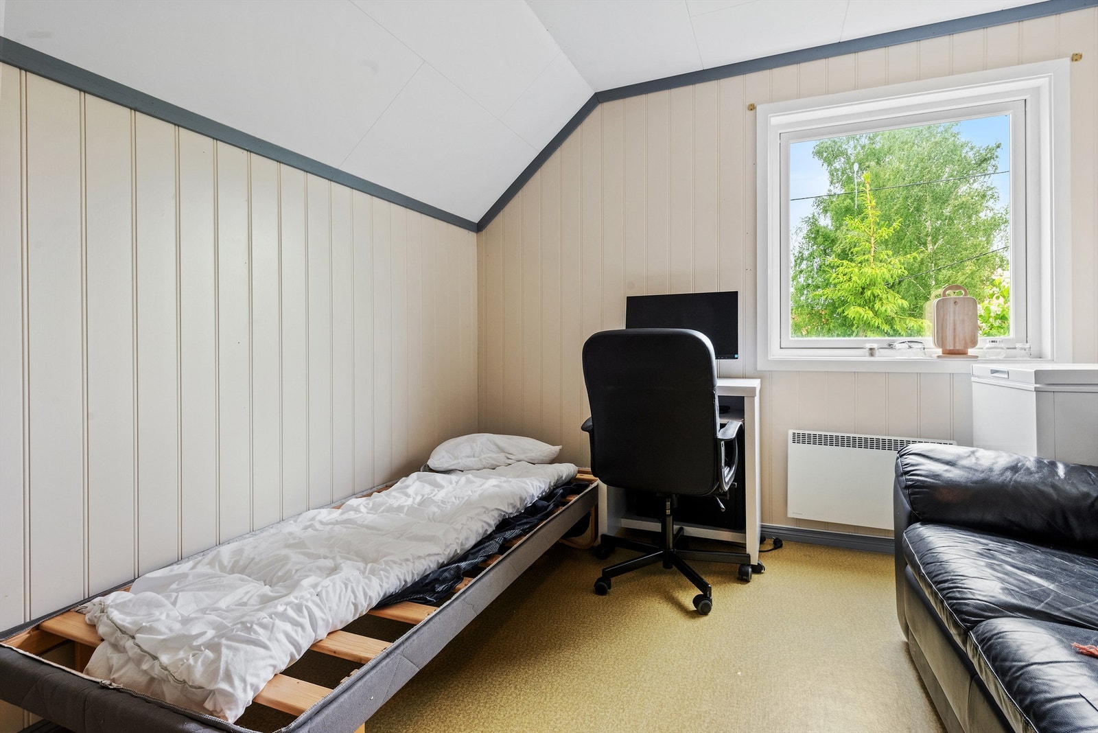 Det andre soverommet i 2. etasje med lysmalt panel på veggene og belegg på gulvet. Rommet har panelovn montert på veggen som varmekilde. Galleribilde