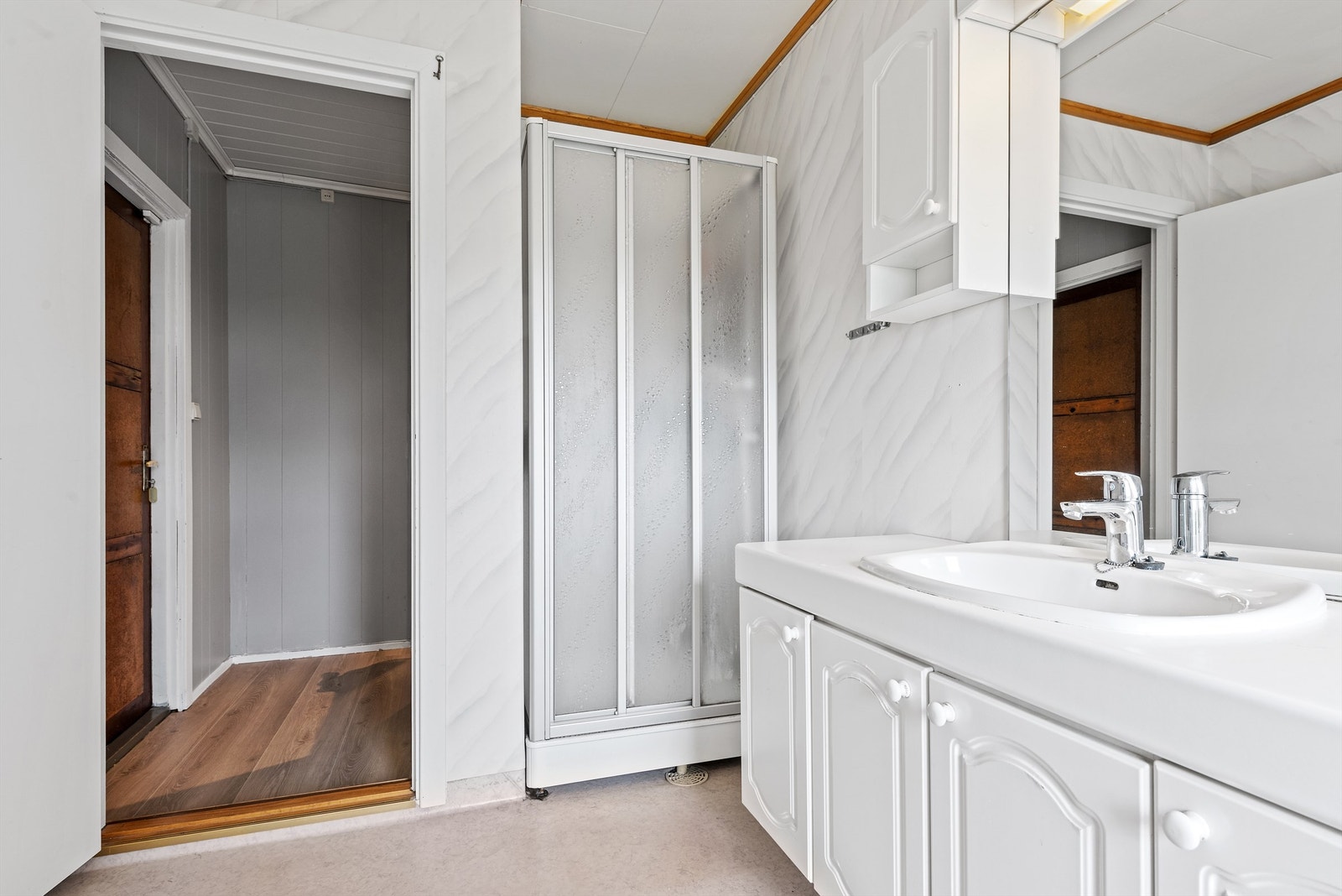 Badet er innredet med servant i skapinnredning med profilerte fronter, overskap, speil og lysarmatur, gulvmontert wc, dusjkabinett og opplegg for vaskemaskin og tørketrommel. Galleribilde