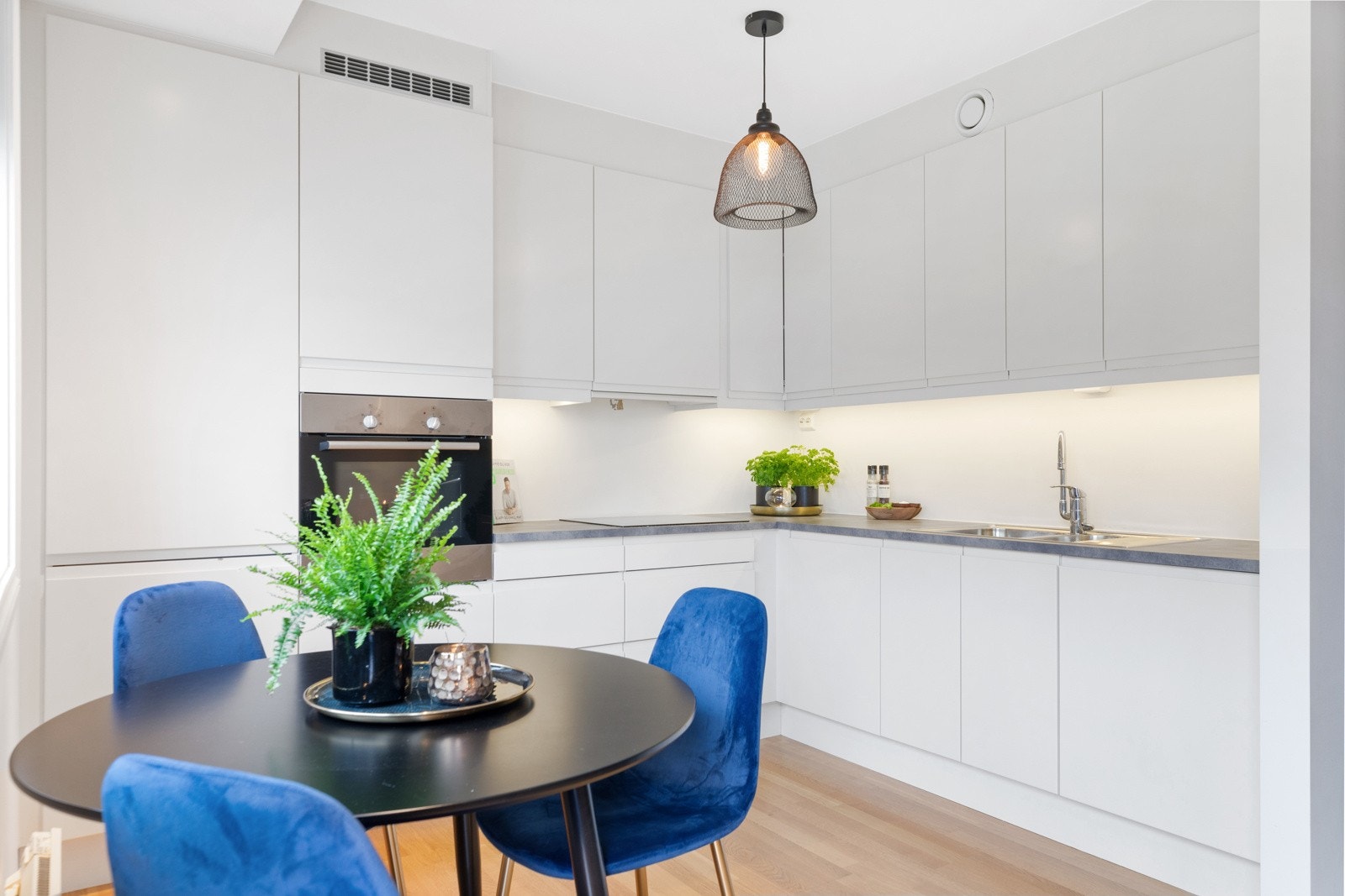 Kjøkkeninnredningen har en moderne stil med glatte, håndtaksløse fronter og grå laminatbenkeplate. Galleribilde